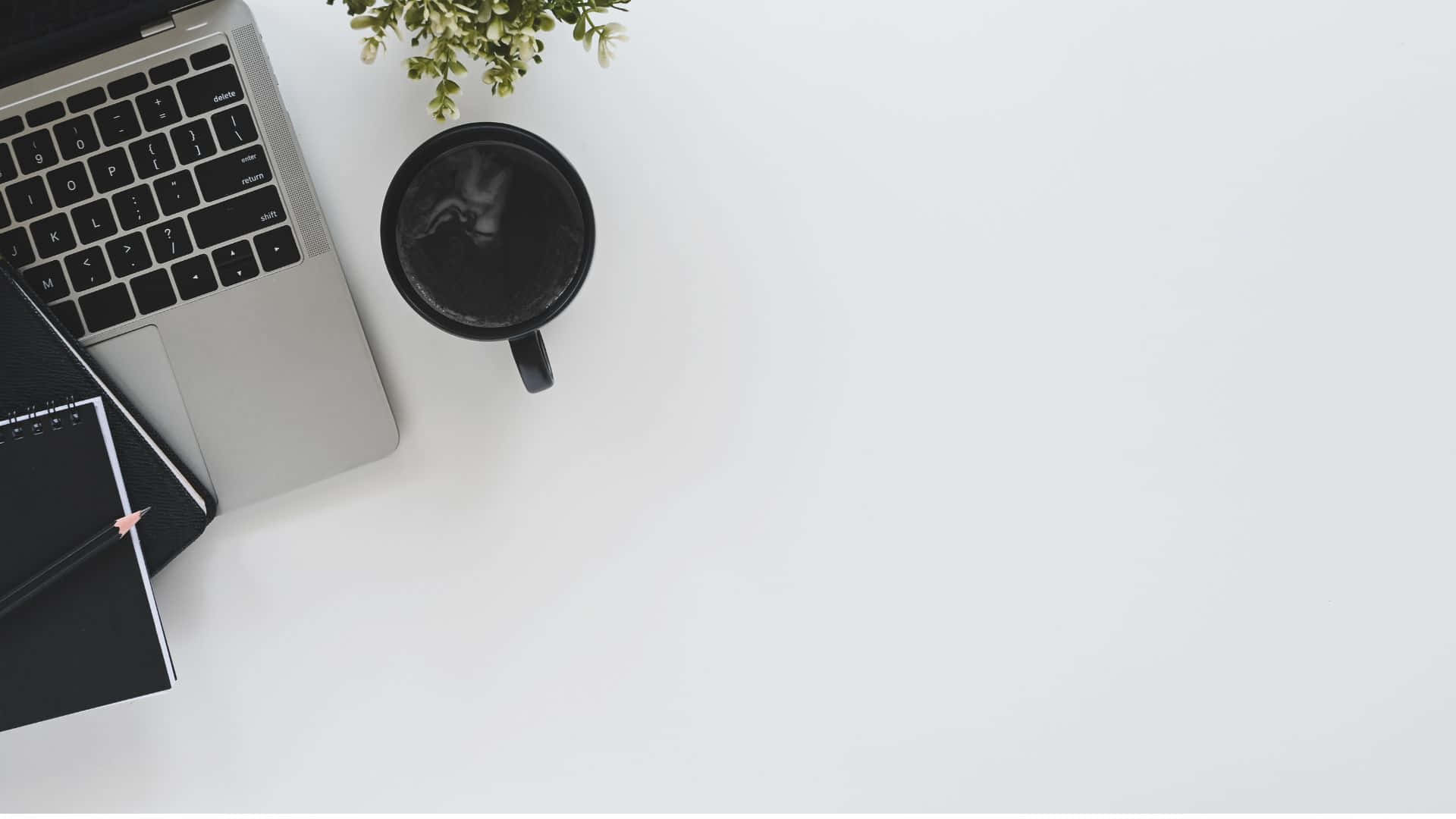 1920 X 1080 桌布 壁紙 — 從上方俯瞰簡約白色書桌，配有銀色筆記型電腦、黑色馬克杯和小型綠色植物。