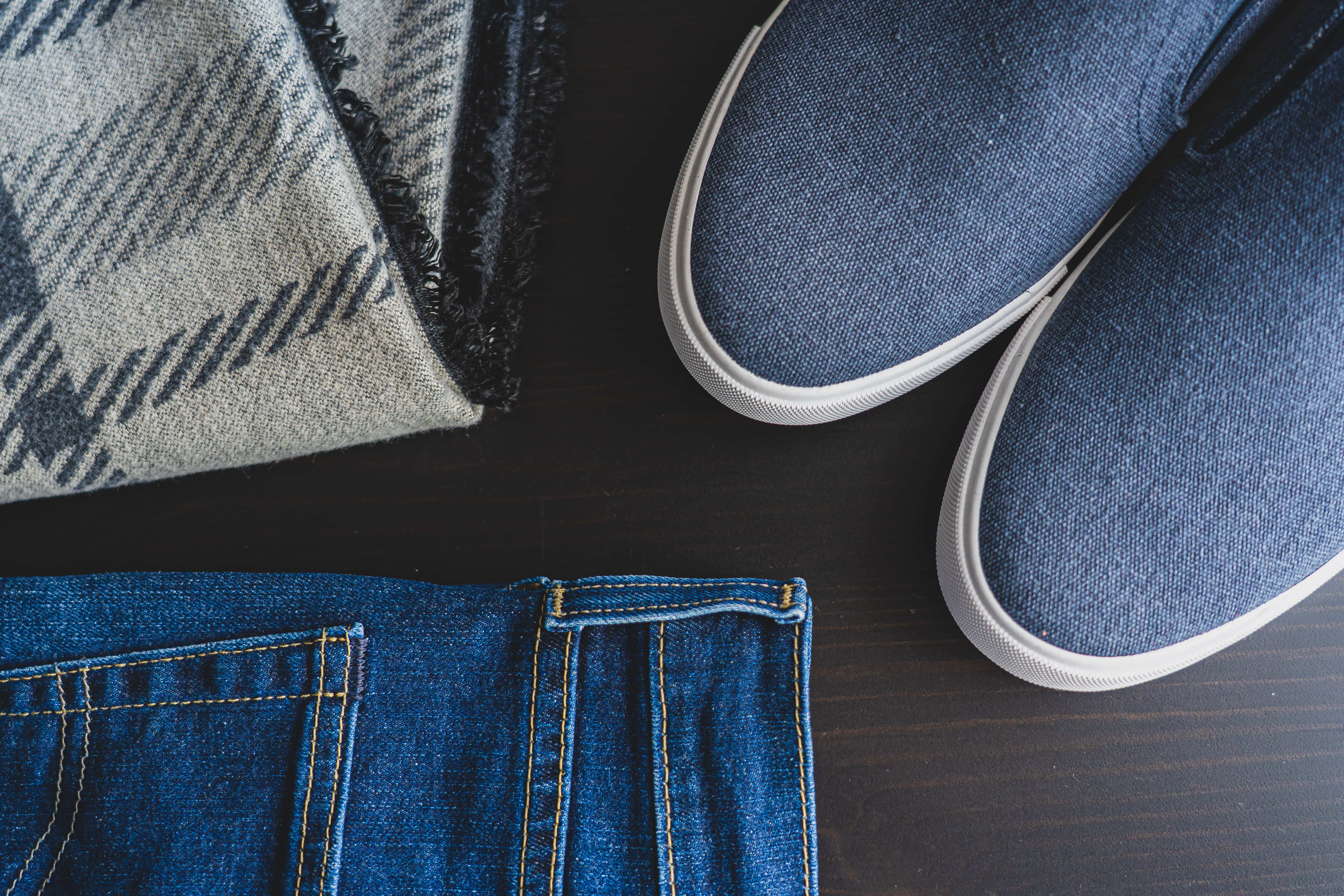 Navy Blue Shoes 桌布 壁紙 — 從上方俯瞰藍色牛仔褲口袋、藍色 slip-on 運動鞋和灰色格紋圍巾擺放在深色木質表面上的景象。