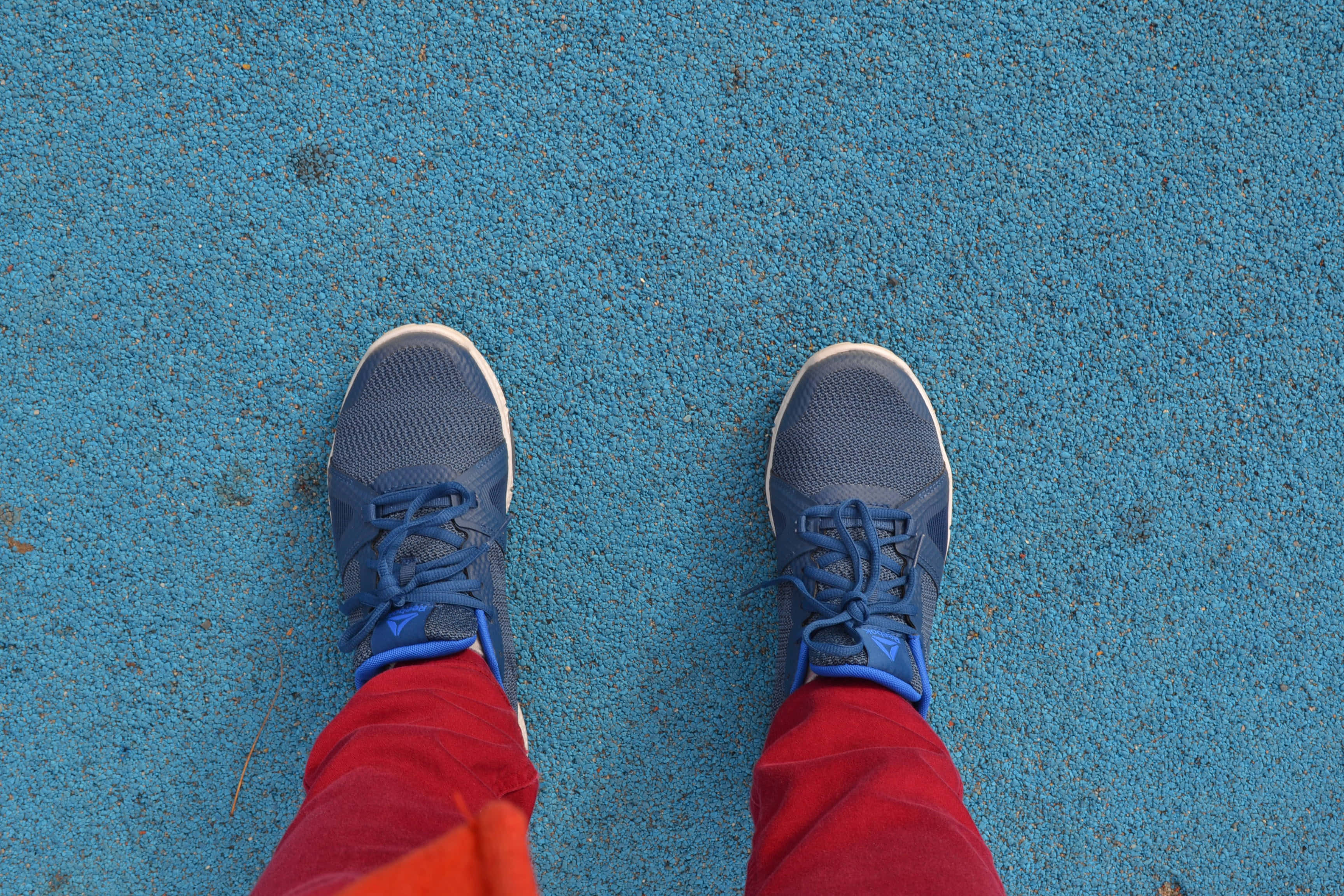 Navy Blue Shoes 桌布 壁紙 — 從上方俯瞰藍色運動鞋和紅色褲子站在有紋理的藍色路面上。