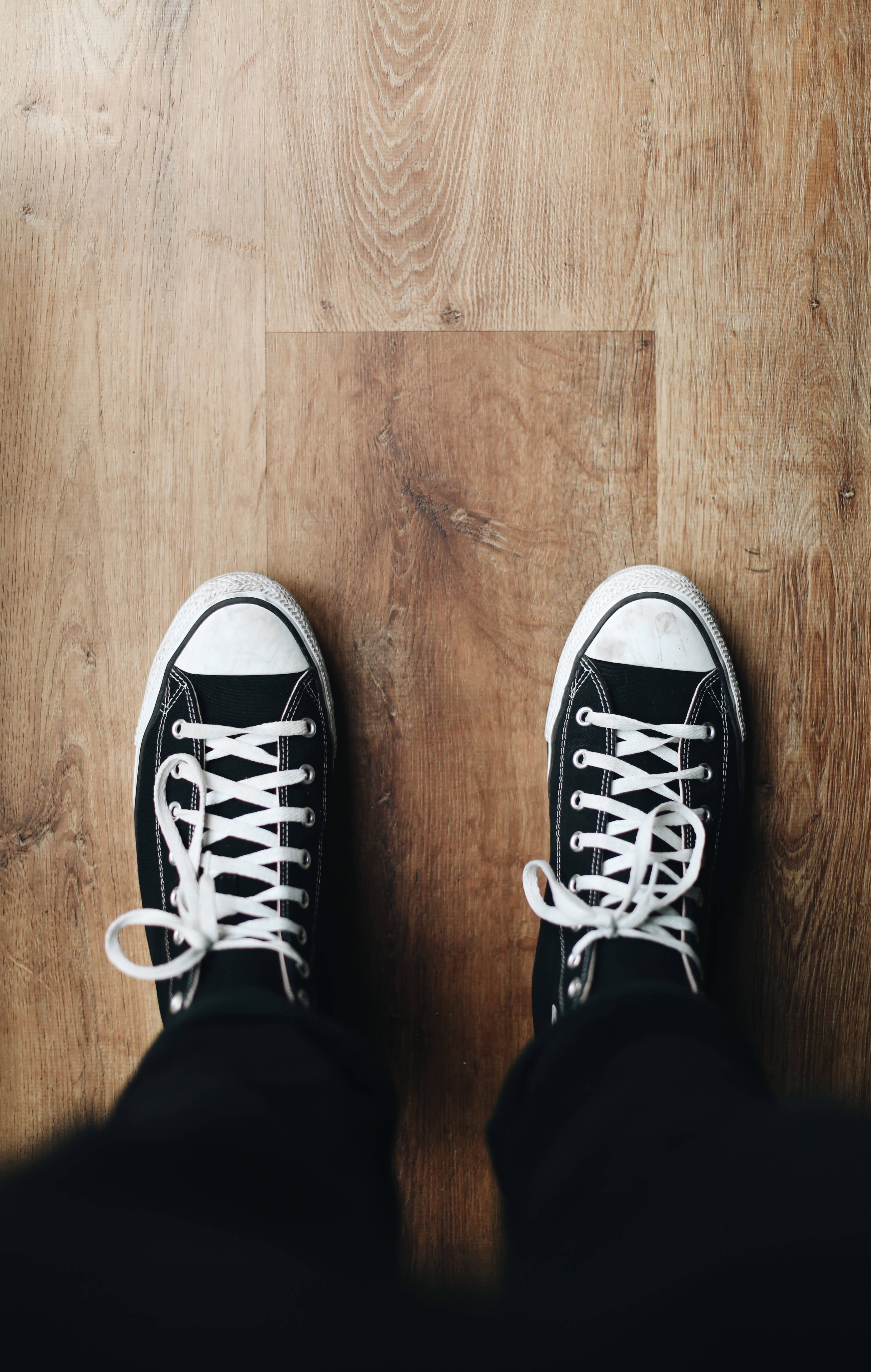 Converse 桌布 壁紙 — 從上方俯瞰黑白運動鞋放在暖色調木地板上，可見木紋圖案。