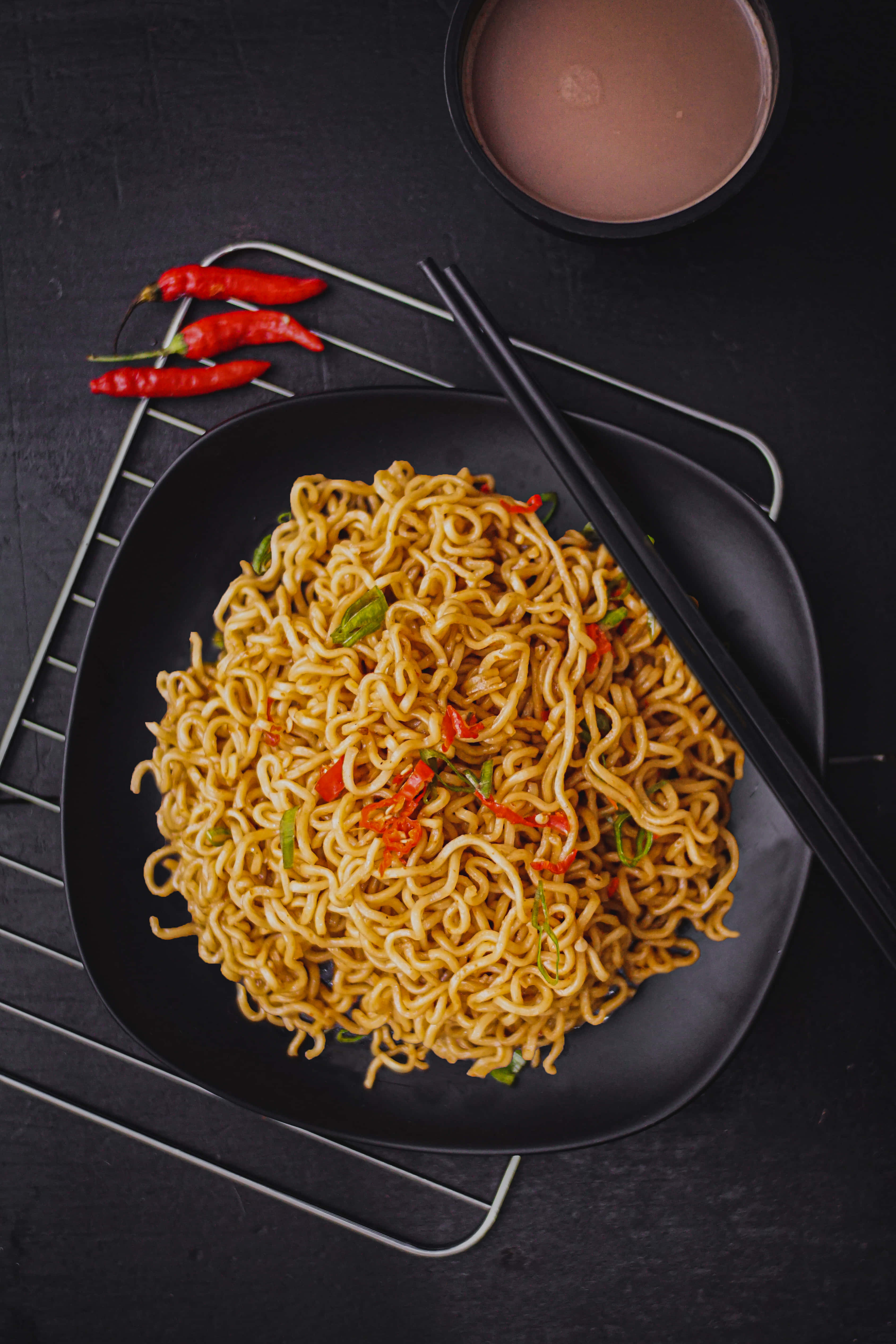Noodles 桌布 壁紙 — 從上方俯瞰黑色碗中的辛辣即食麵，搭配筷子與紅辣椒，置於深色紋理表面上。