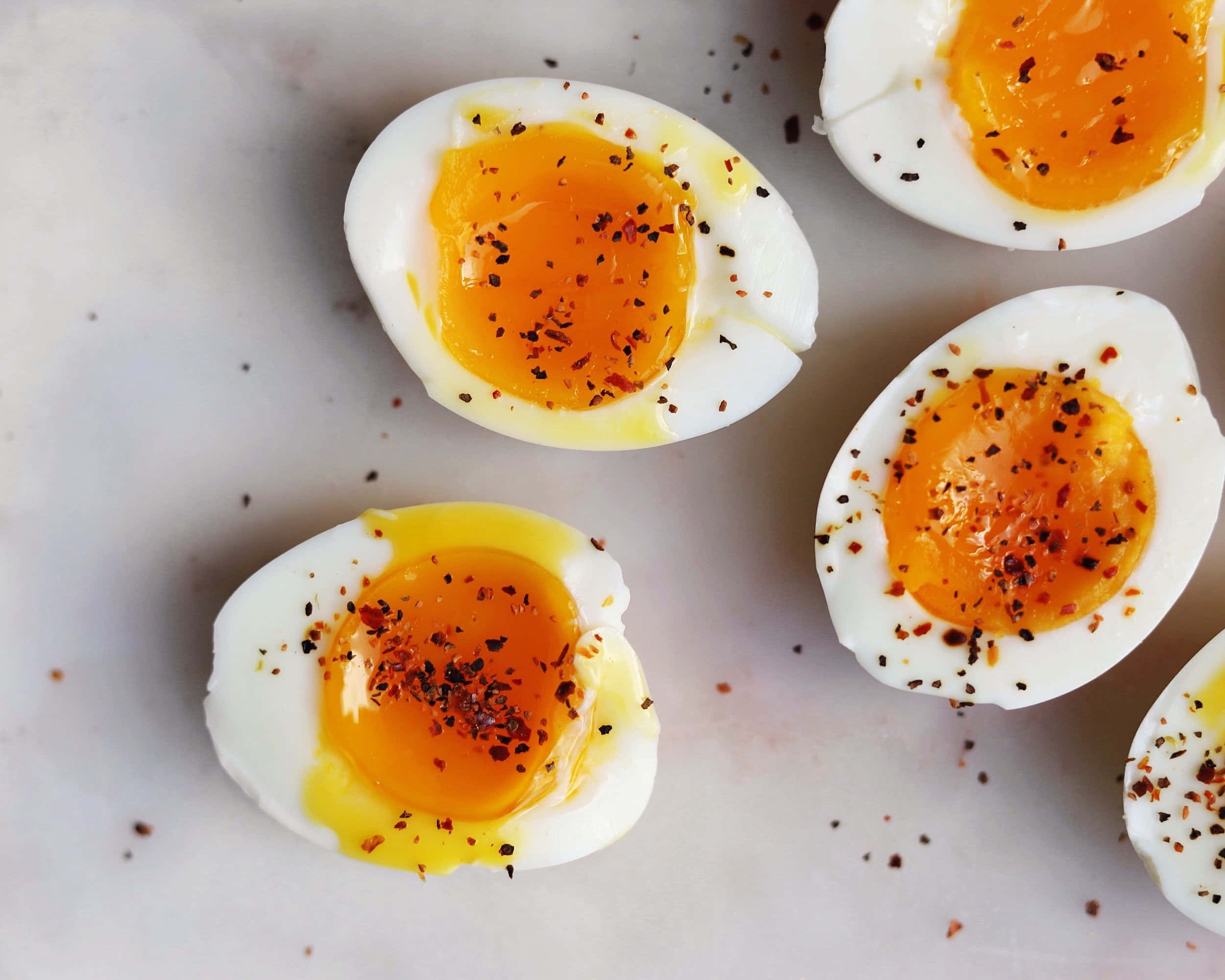 Egg 桌布 壁紙 — 從上方拍攝半熟水煮蛋切半，流出蛋黃，配上紅辣椒片，置於大理石表面。