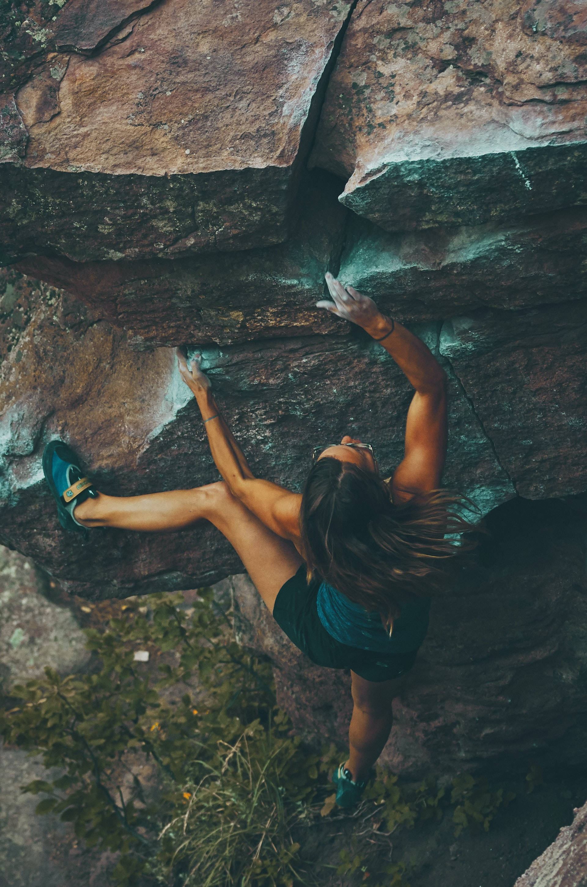 Climbing 桌布 壁紙 — 從上方視角看，一名攀岩者攀登崎嶇的岩壁，下方是茂密的綠色植物。