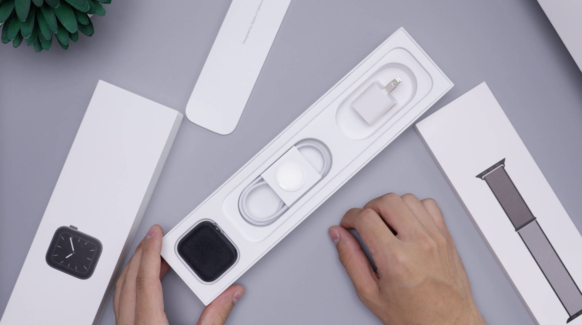 雙手在灰色表面上拆開Apple Watch，附有充電器和錶帶。 — 智慧手錶 GIF 壁紙