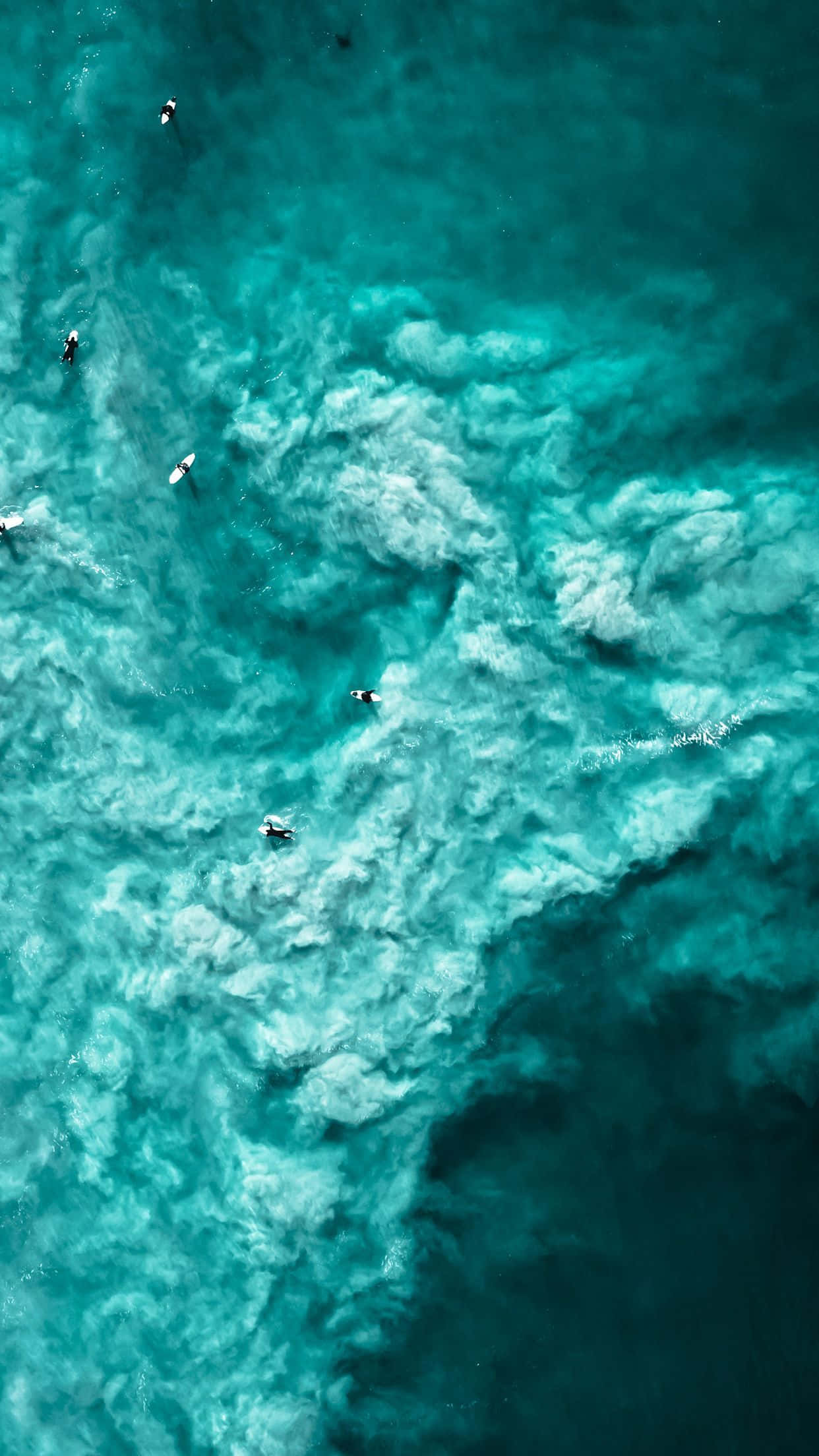 桌布 壁紙 — 從上空俯瞰衝浪者在帶有白色泡沫圖案的碧綠海浪上衝浪。