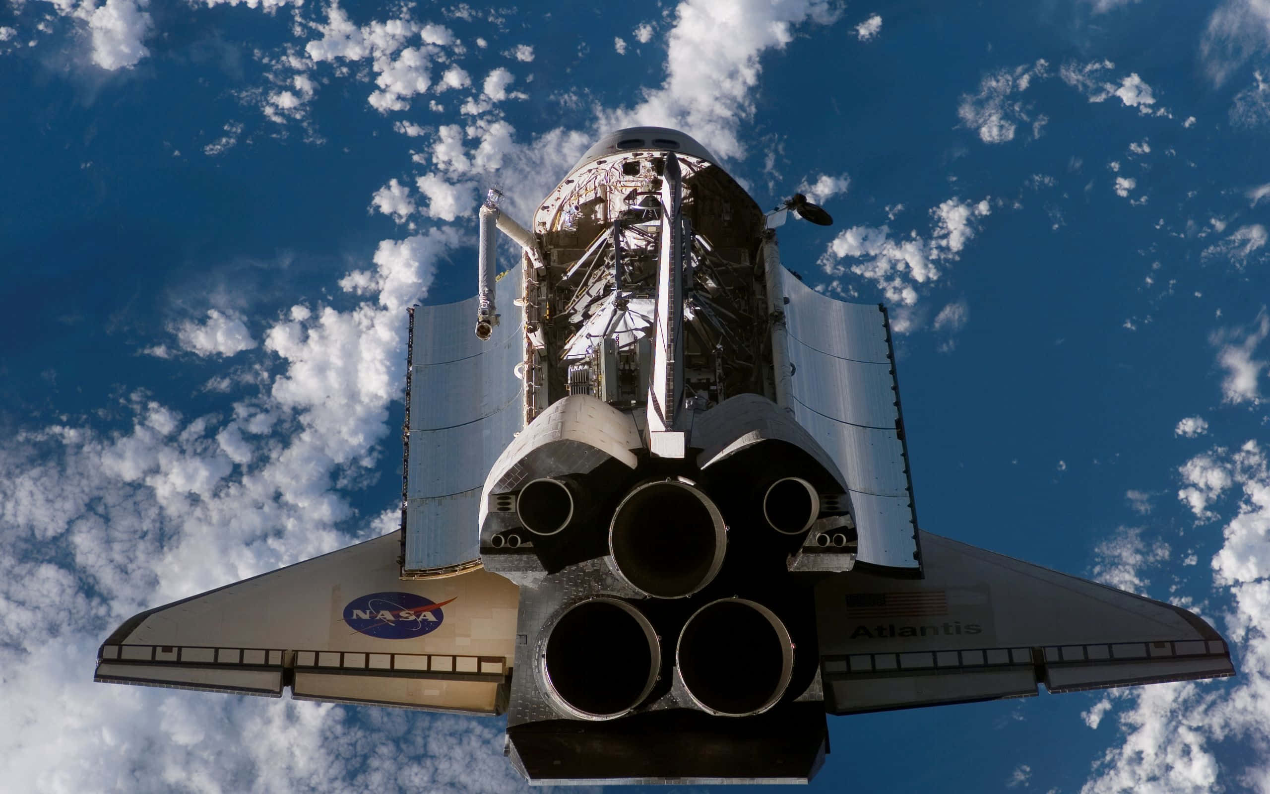 space shuttle 桌布 壁紙 — 從下方仰望亞特蘭提斯號太空梭，背景是湛藍的天空和散落的白雲。