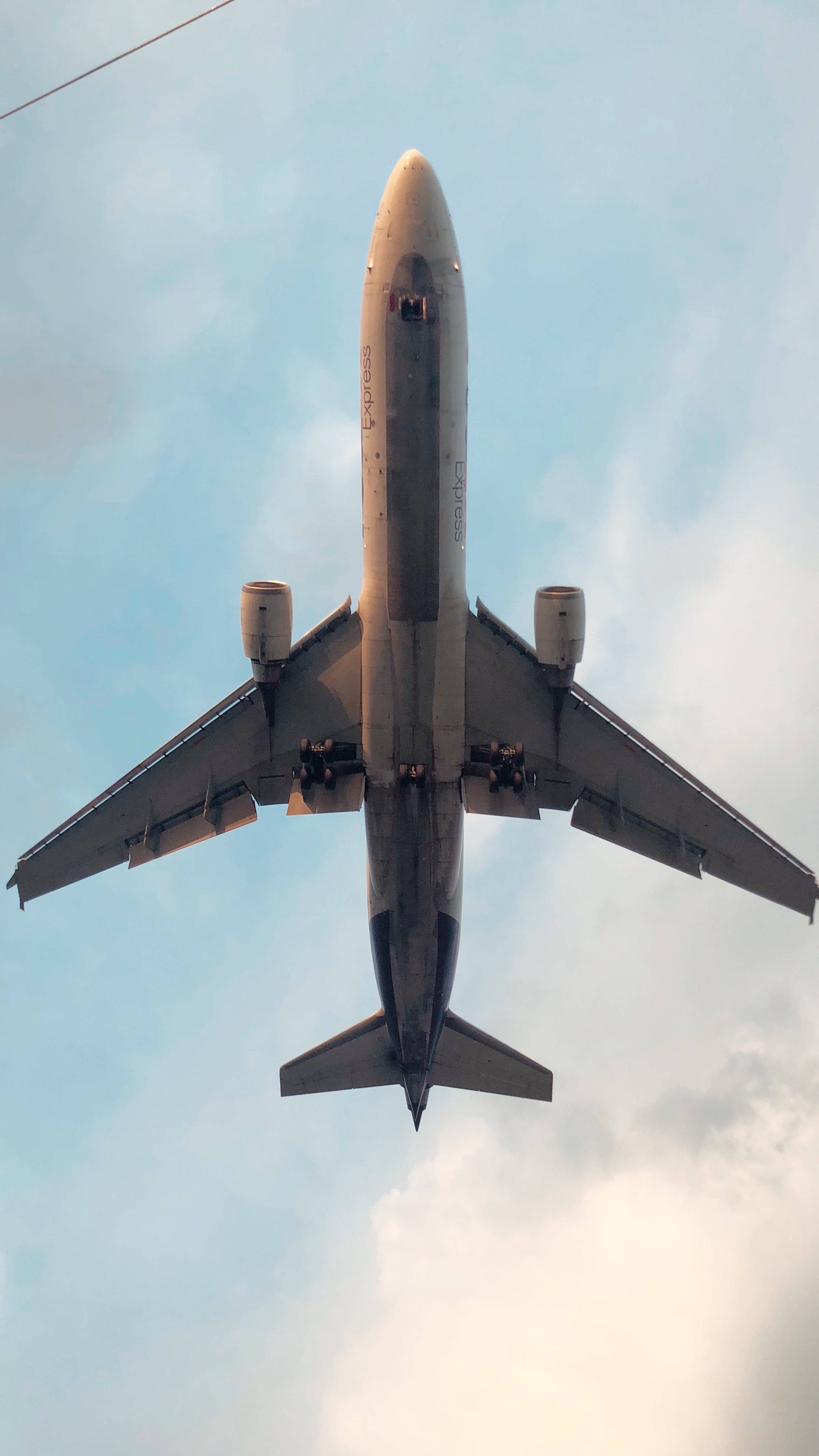 飛機 桌布 壁紙 — 從下方觀看一架商用飛機在頭頂飛過，背景是柔和藍天，點綴著零星雲朵。