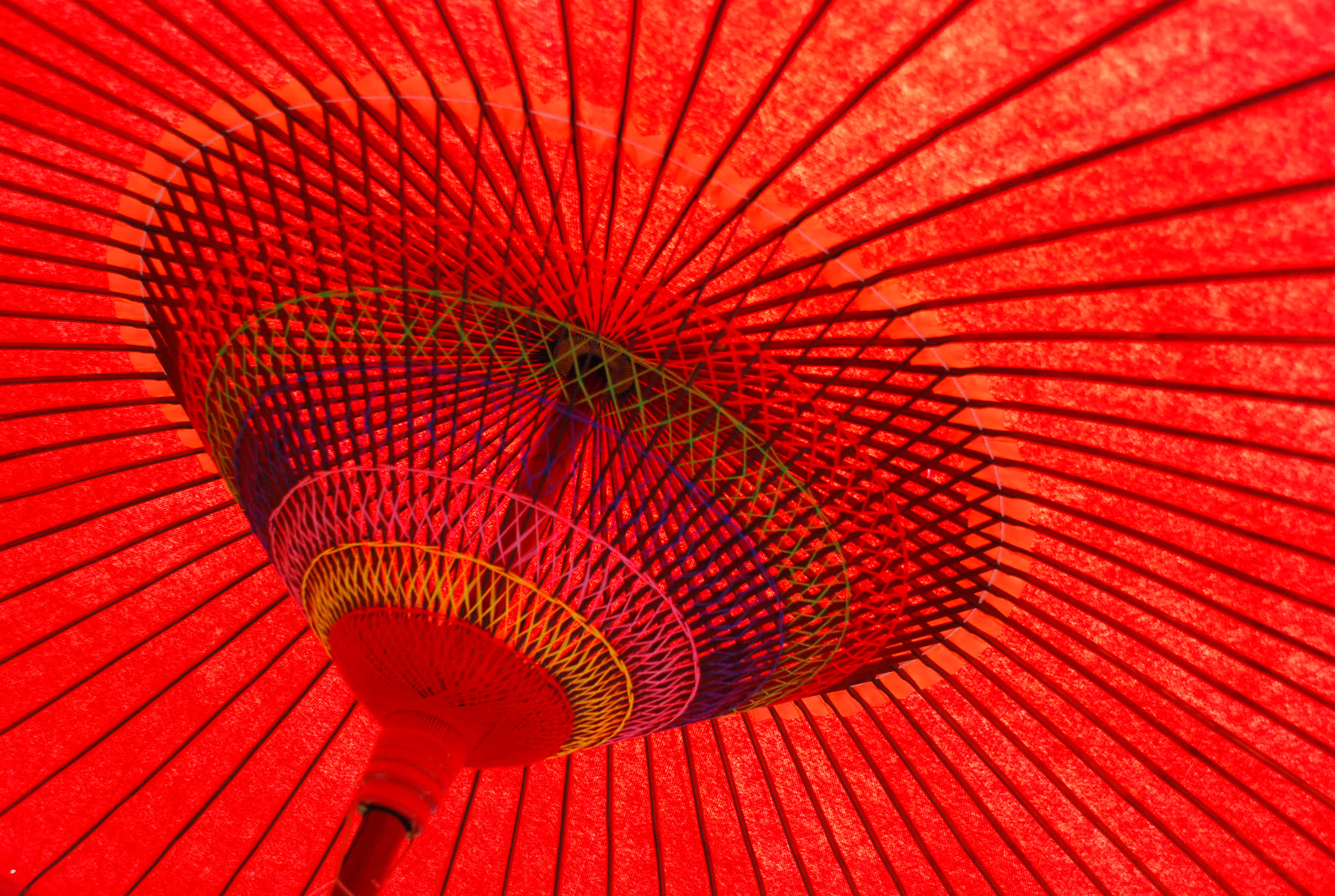 Red Japanese 桌布 壁紙 — 從下方觀看的鮮紅色傳統雨傘，展現精緻的竹骨和色彩繽紛的編織細節。