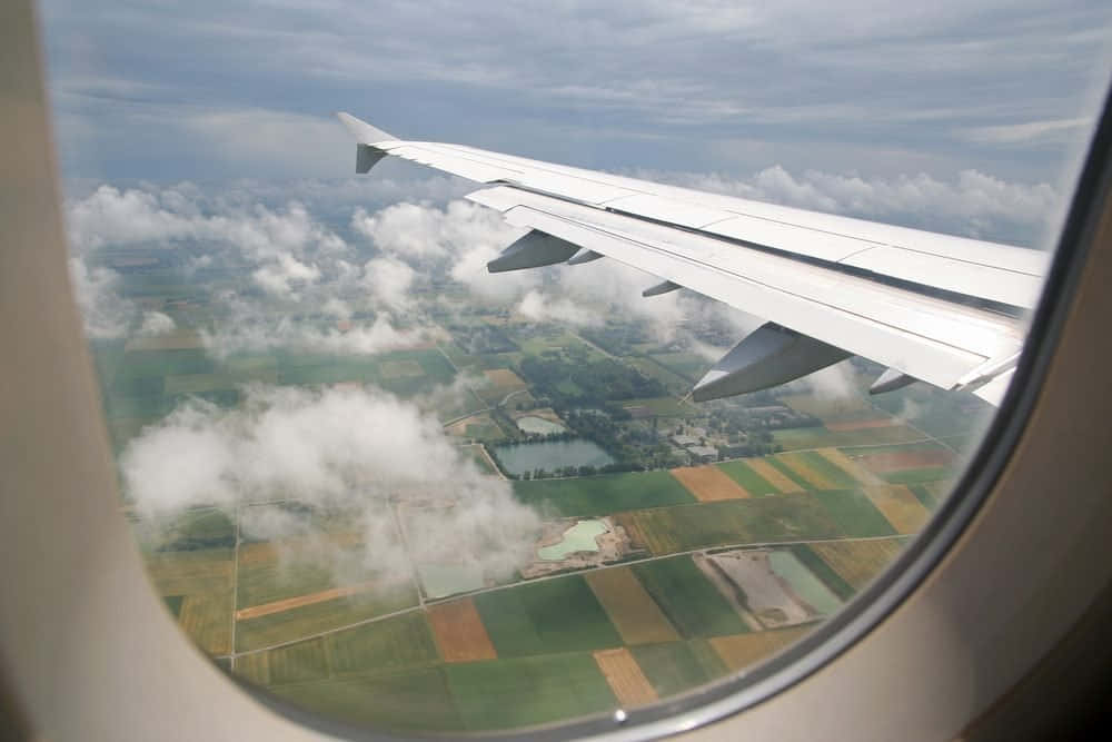 Airplane Window 桌布 壁紙 — 從乘客窗戶看到的飛機機翼，俯瞰下方拼布般的農田和零星雲朵。