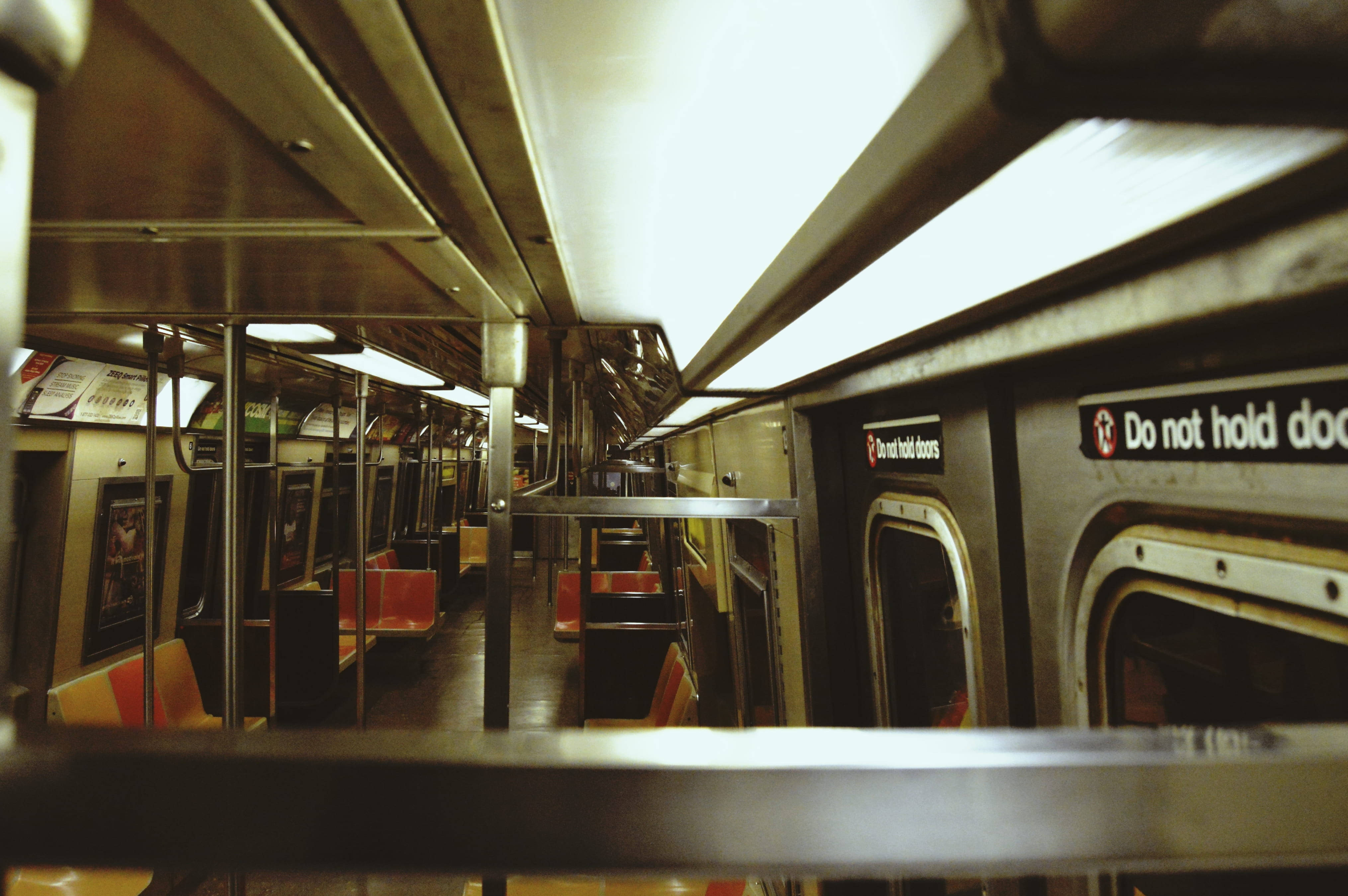 Subway 桌布 壁紙 — 從低角度俯瞰地鐵車廂空蕩的金屬內部，設有橙色座椅和散發溫暖光芒的頂燈。