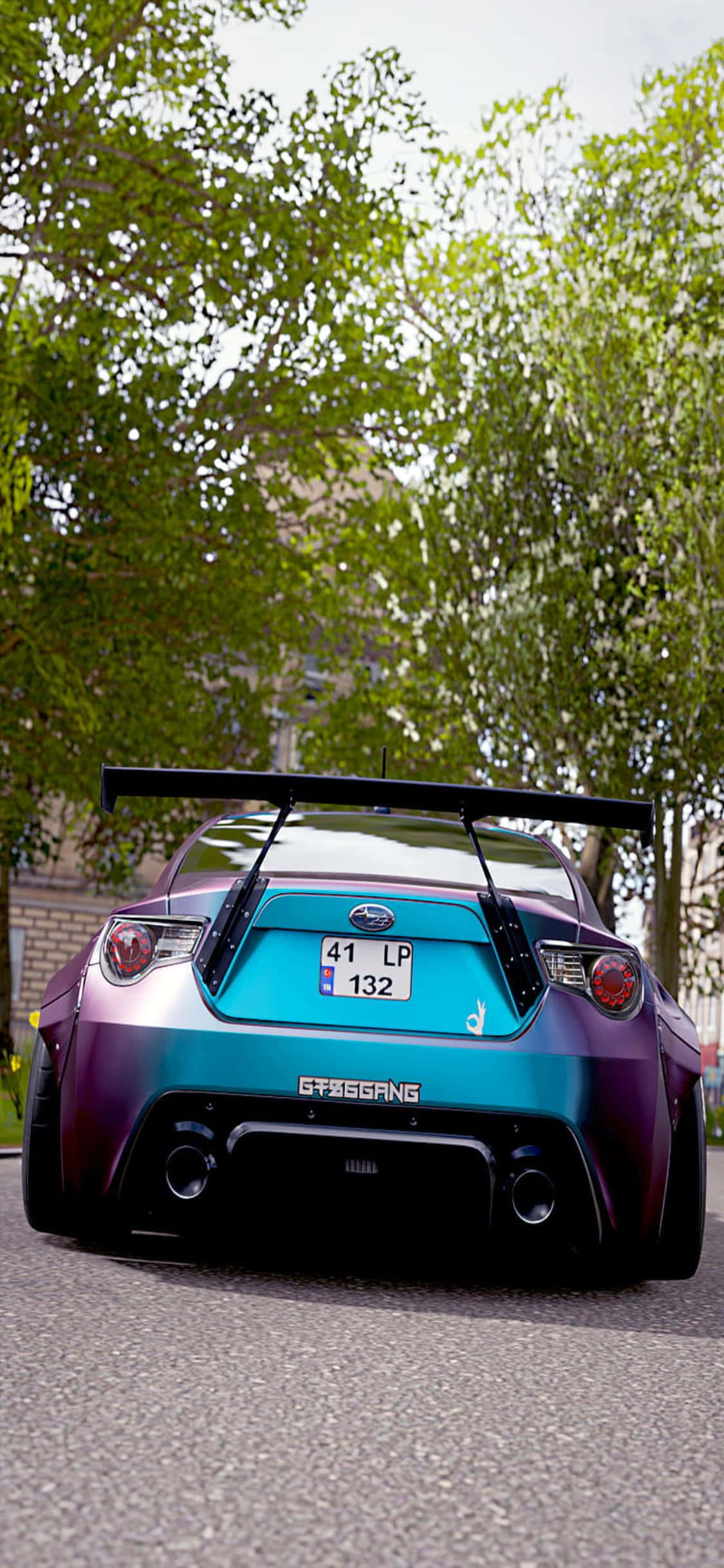 iPhone Xs Forza Horizon 4 桌布 壁紙 — 從低角度後方觀看一輛鮮豔紫色和藍綠色的改裝跑車，帶有大型尾翼，停泊在綠樹成蔭的街道上。