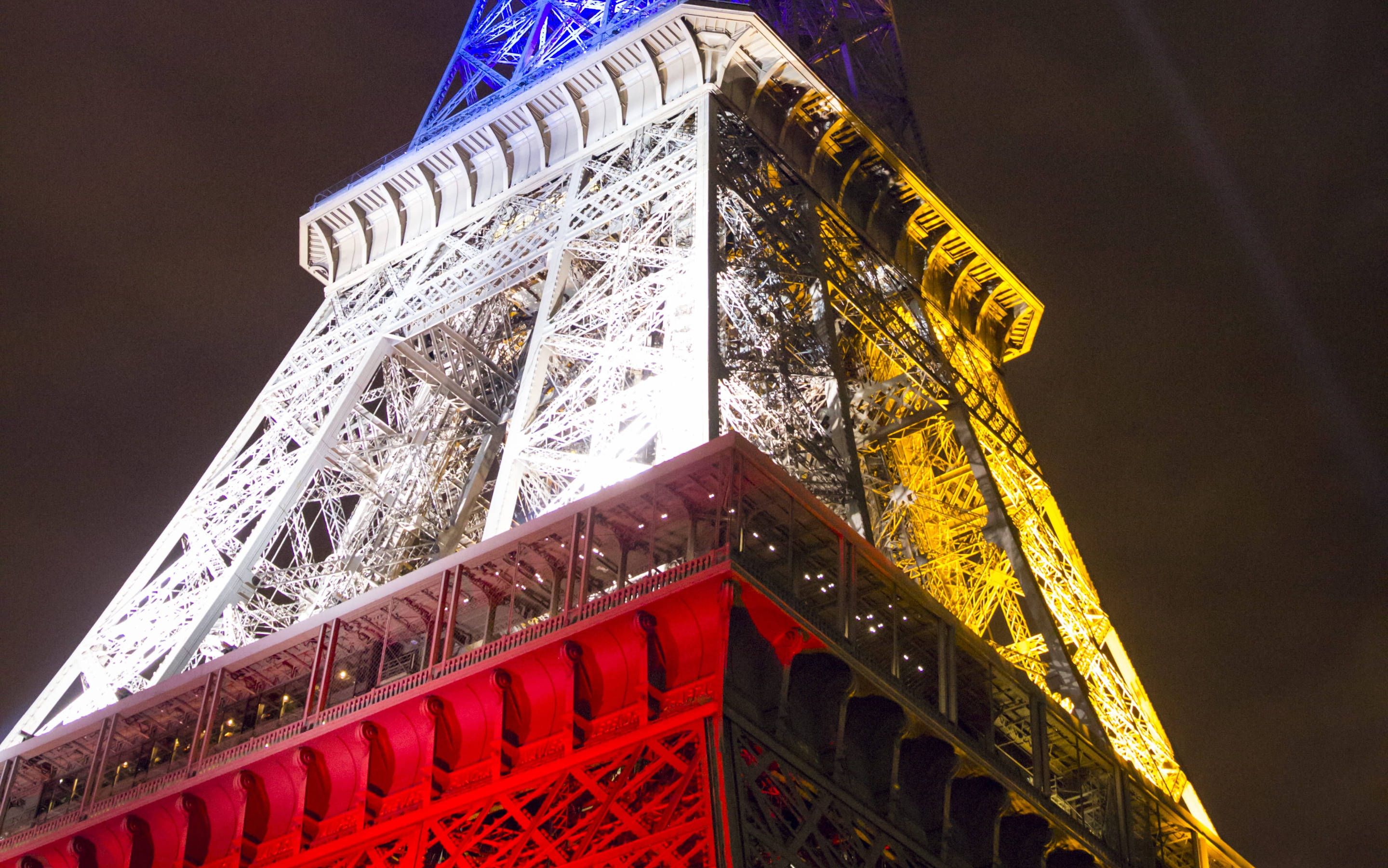 France Flag 桌布 壁紙 — 從低角度拍攝，艾菲爾鐵塔在漆黑的夜空下閃耀著紅、黃、藍三色燈光。