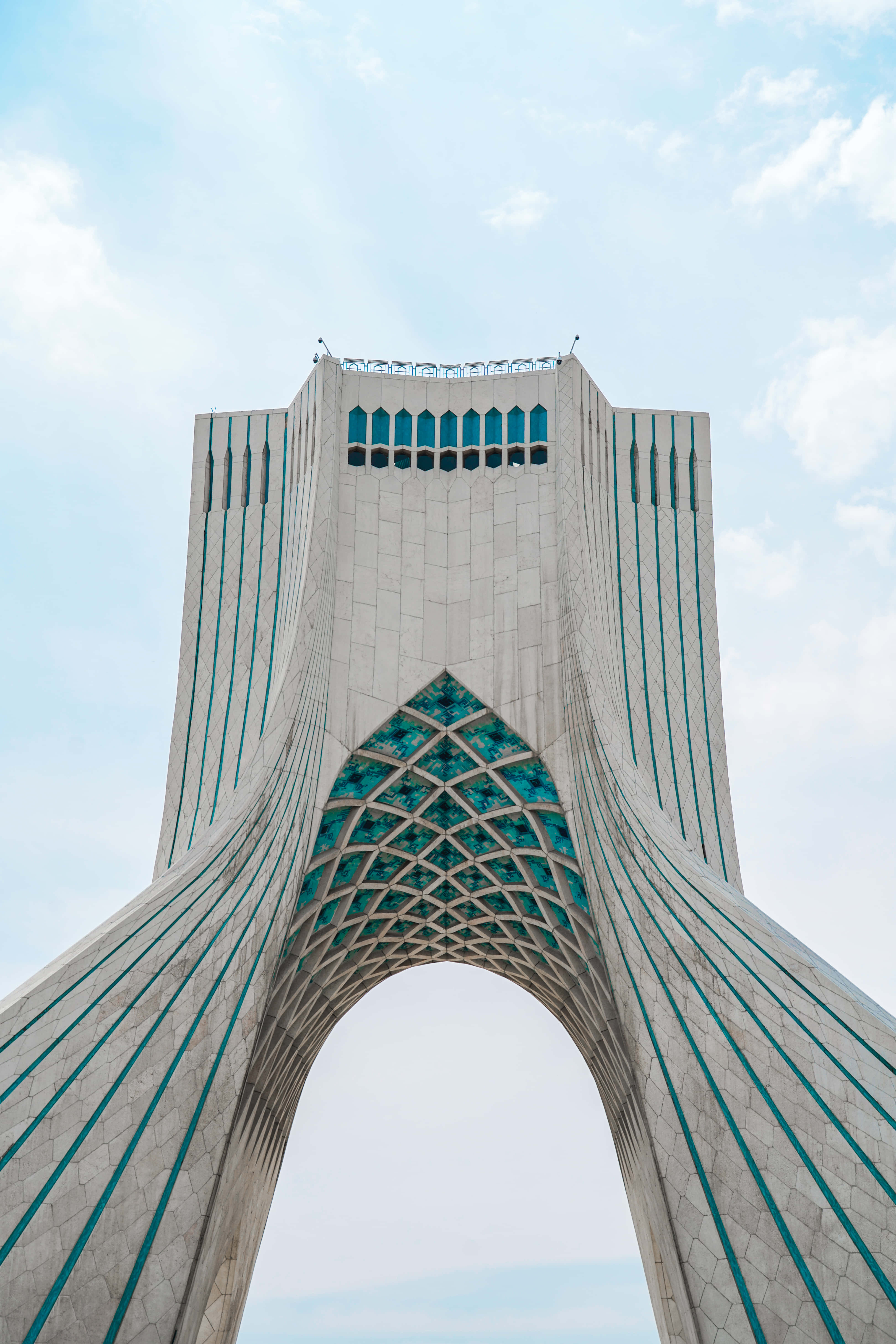 Iran 桌布 壁紙 — 從低角度拍攝的德黑蘭阿扎迪塔，展示其標誌性拱門和綠松石玻璃工藝，背景是明亮的藍天。