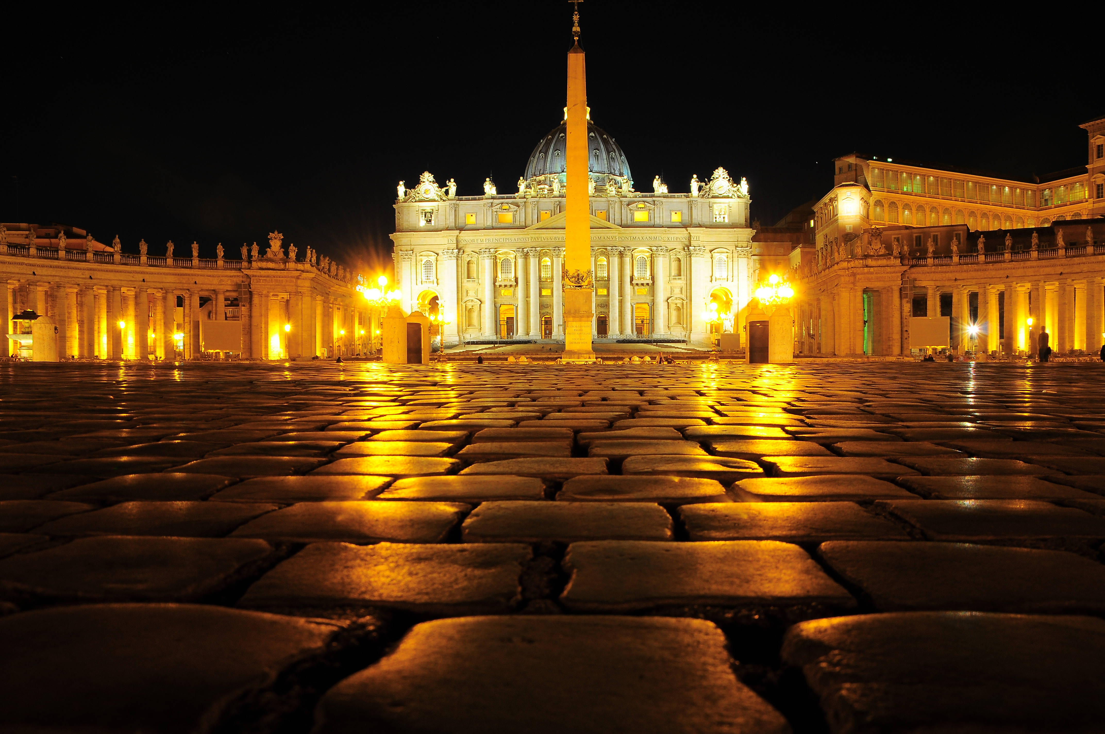 Vatican 桌布 壁紙 — 從低角度拍攝的梵蒂岡聖彼得大教堂夜景，金色燈光映照在濕漉漉的鵝卵石上。