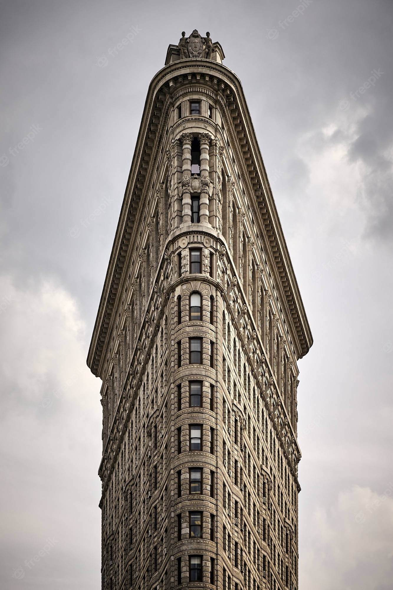 Flatiron Building 桌布 壁紙 — 從低角度拍攝紐約市標誌性熨斗大廈刺穿多雲灰天的戲劇性景觀。