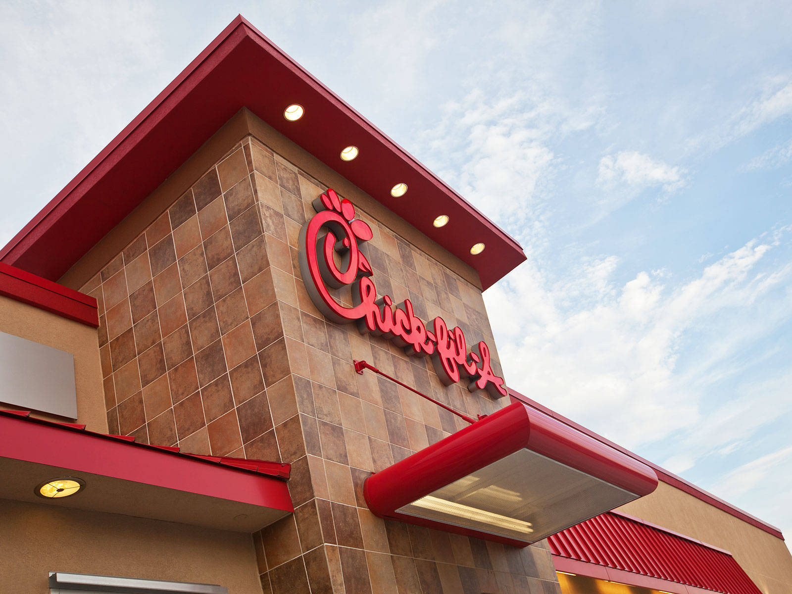 chick 桌布 壁紙 — 從低角度觀看Chick-fil-A餐廳，紅色飾邊和標誌襯托著部分多雲的藍天。