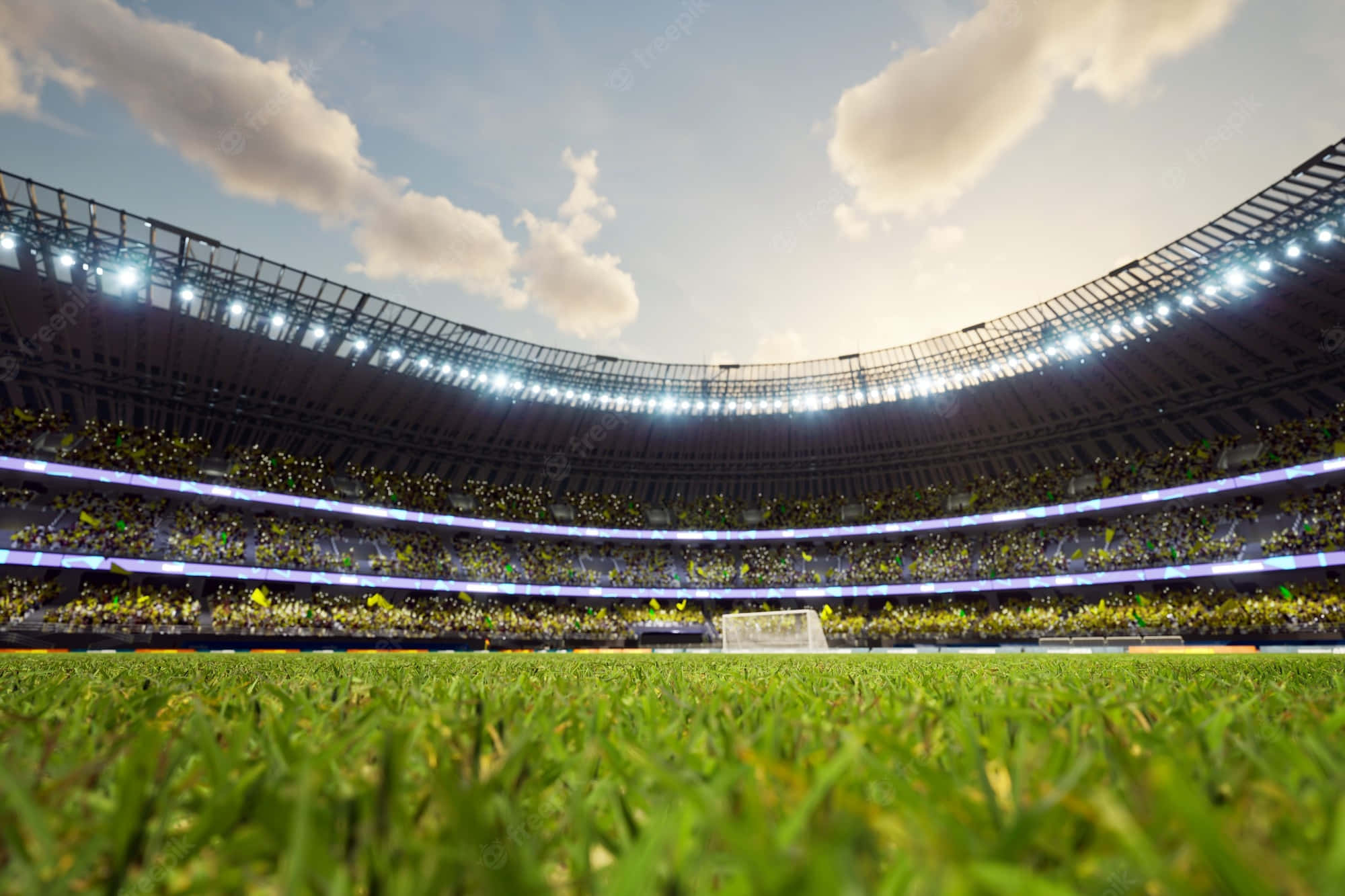 Soccer Stadium 桌布 壁紙 — 從低角度觀看一個充滿活力的綠色足球場，位於一個巨大的體育場內，場內擠滿了在明亮燈光及部分多雲天空下歡呼的球迷。