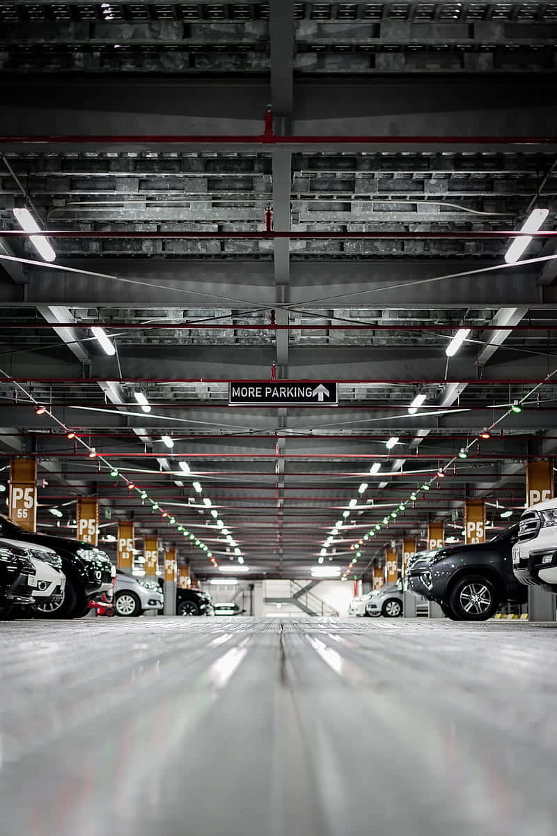 Building 桌布 壁紙 — 從低角度觀看一個寬敞的地下停車場，汽車在明亮的螢光燈下整齊排列。