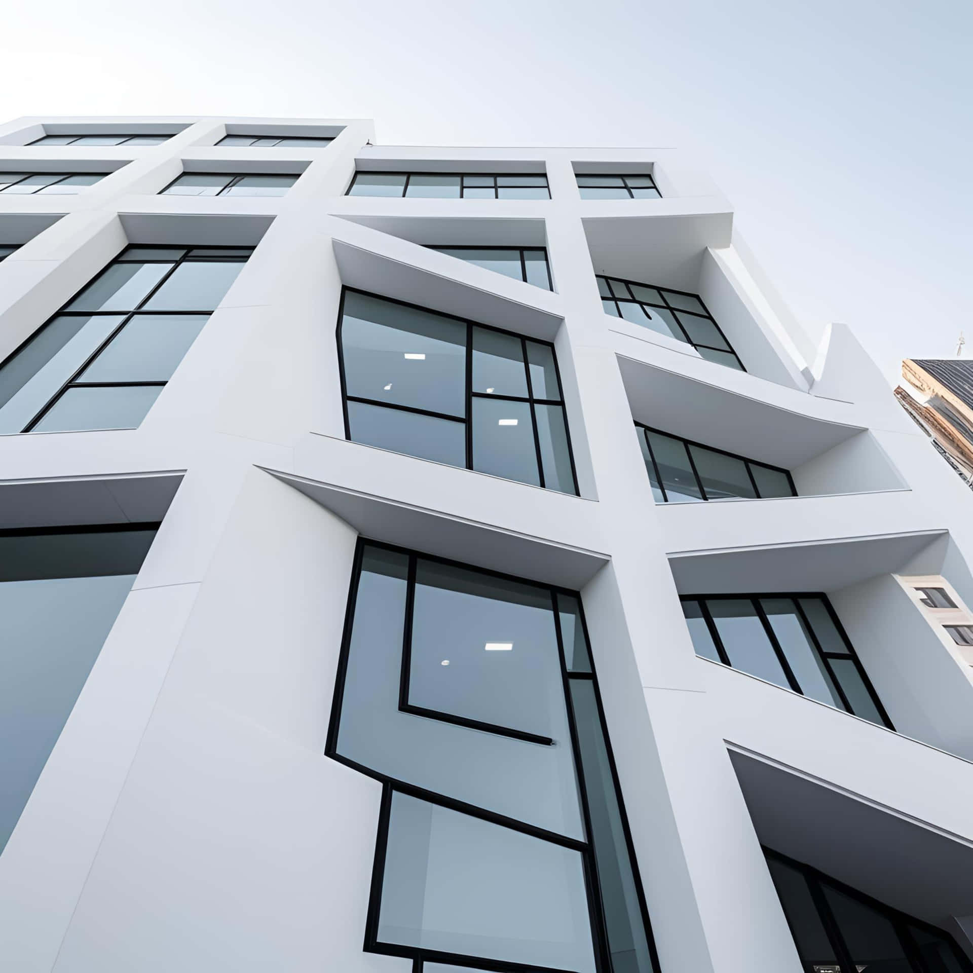 Low angle view of a modern white building with large windows reflecting the blue sky on a sunny day 壁紙 — 從低角度觀看一座現代白色建築，具有大膽的幾何線條和黑色框架窗戶，映襯著蒼白的天空。