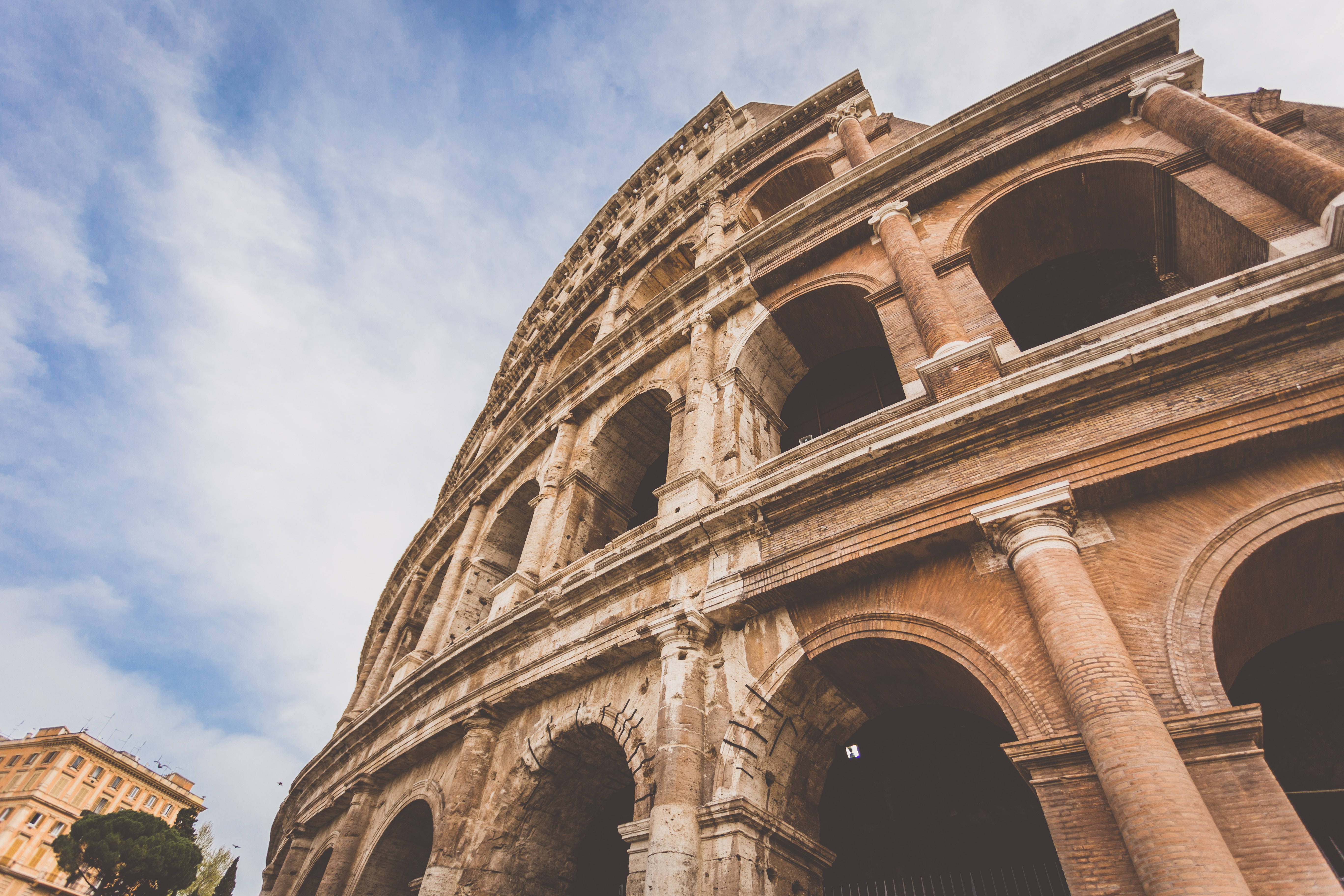 Rome 桌布 壁紙 — 從低角度觀看古羅馬競技場，天空局部多雲，溫暖的陽光突顯其風化的石拱門。