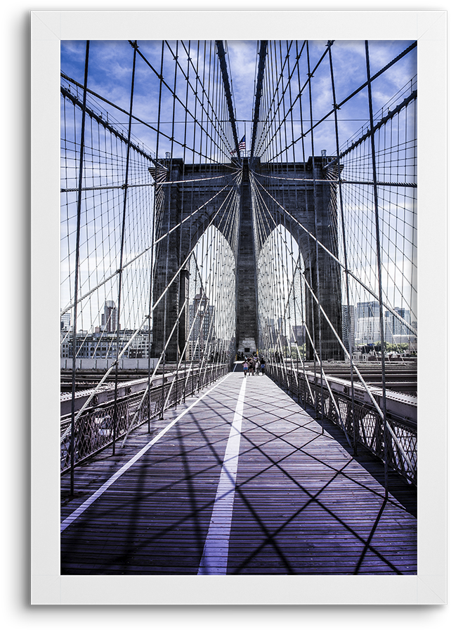Picture Frame 桌布 壁紙 — 從低角度觀看布魯克林大橋，其標誌性的石塔和鋼纜在明亮的藍天下於木製步道上投下幾何陰影。