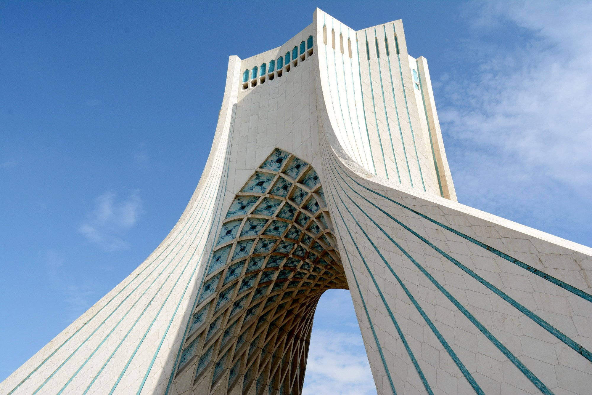 Iran 桌布 壁紙 — 從低角度觀看德黑蘭的阿扎迪塔，其標誌性的白色拱門和藍色玻璃面板映襯著清澈的藍天。