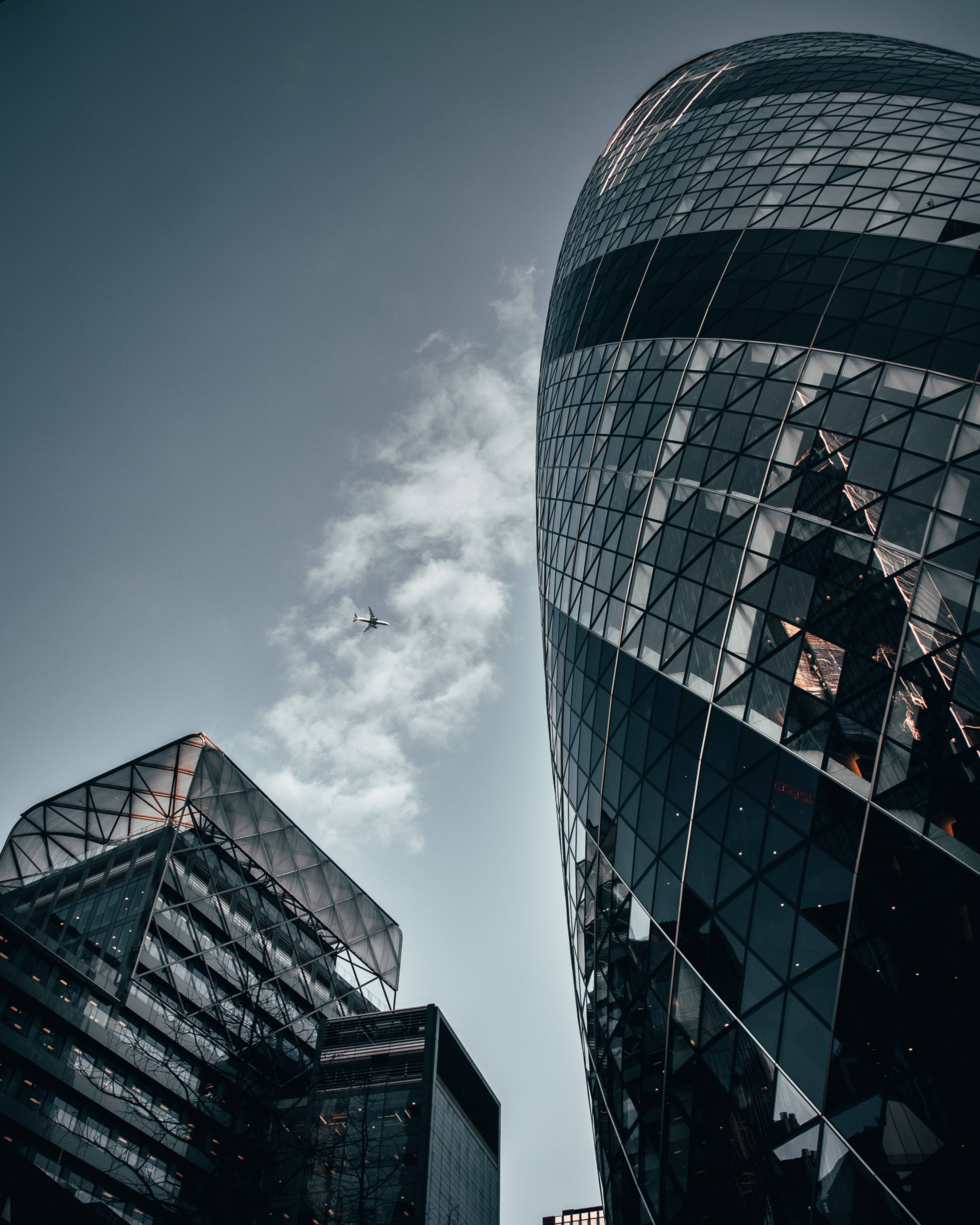 Skyscraper 桌布 壁紙 — 從低角度觀看現代玻璃摩天大樓，天空多雲，遠處有飛機飛過。