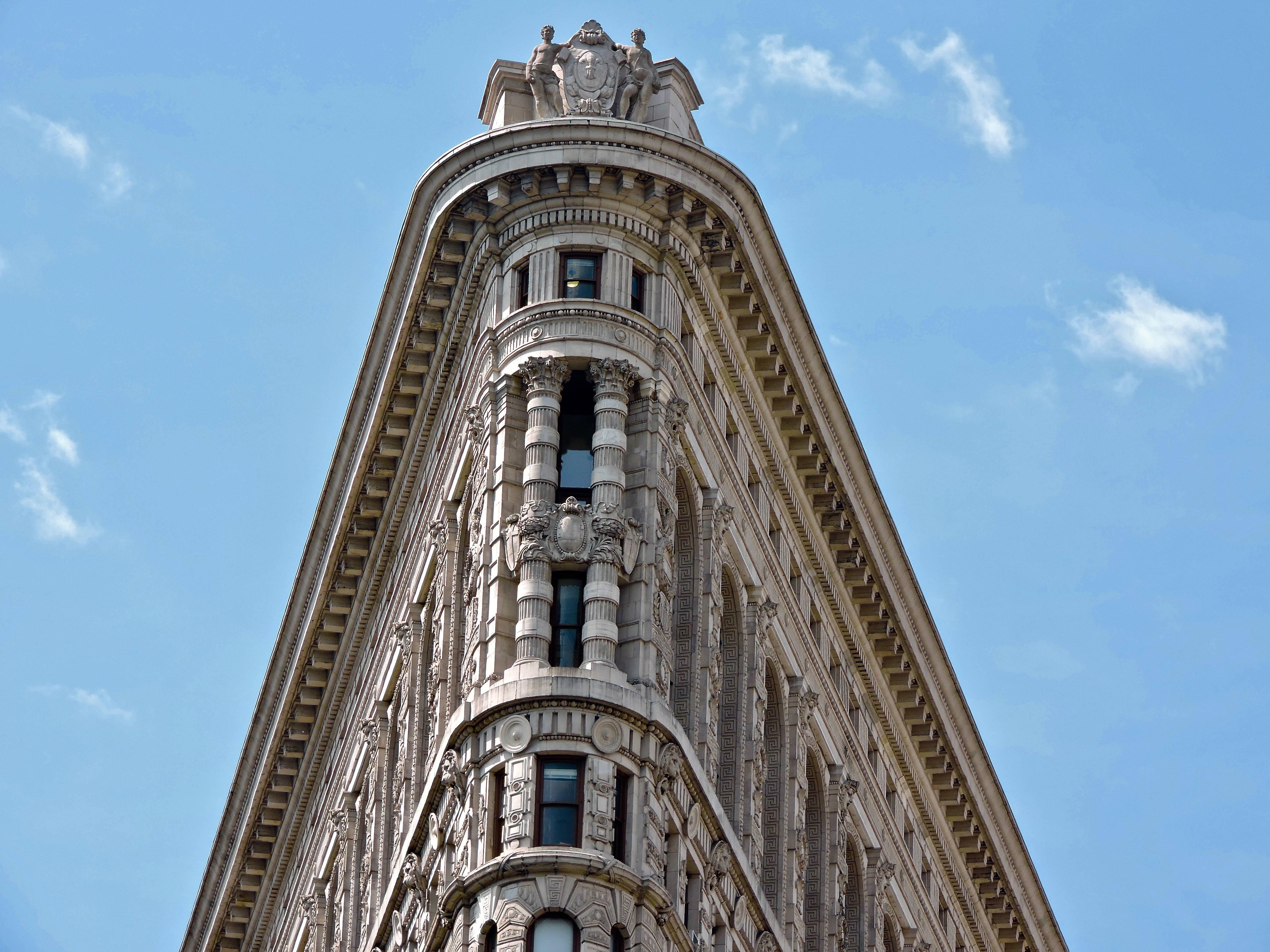 Flatiron Building 桌布 壁紙 — 從低角度觀看紐約市標誌性的熨斗大廈，背景是清澈的藍天和零星的白雲。