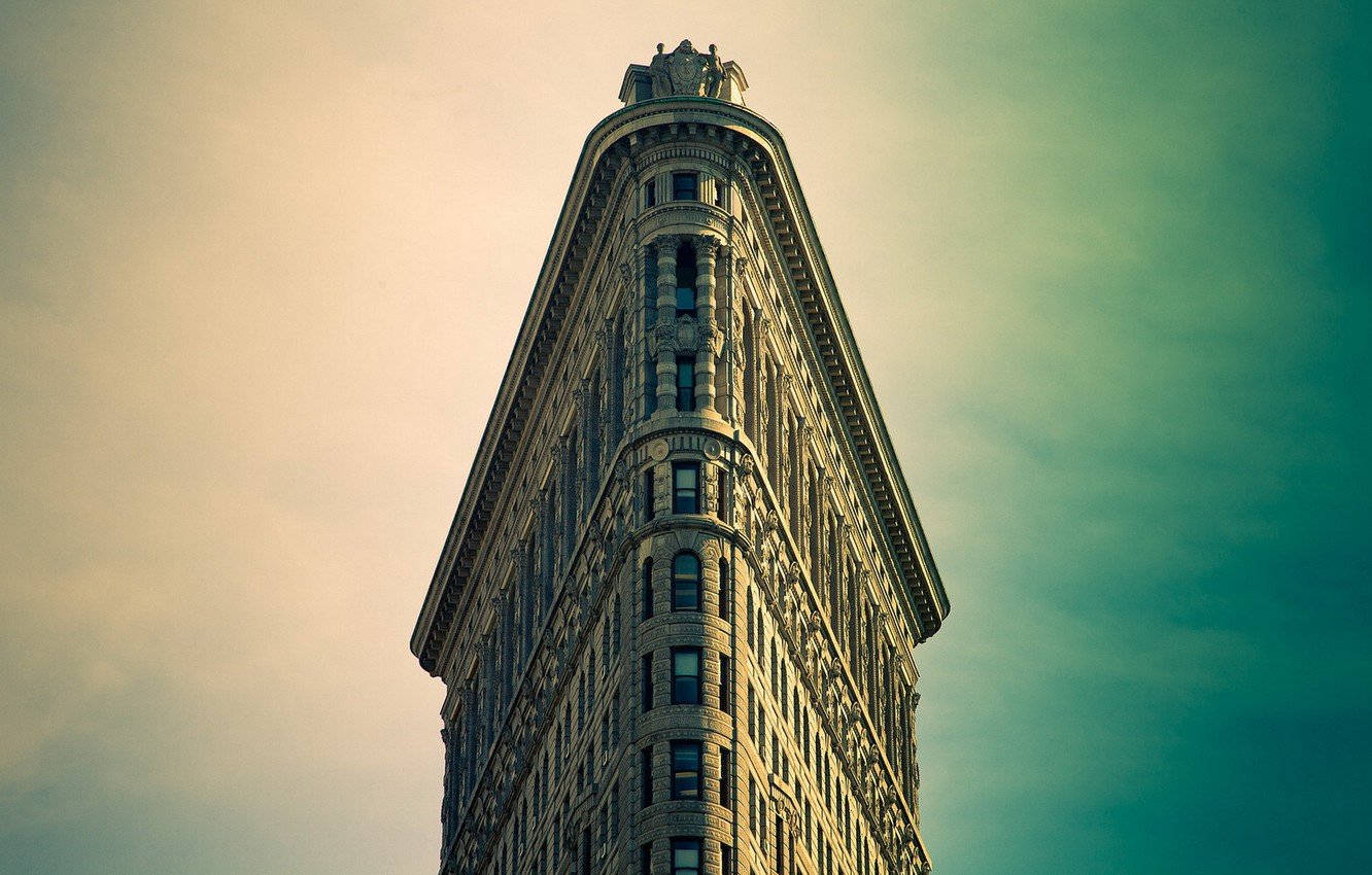 Flatiron Building 桌布 壁紙 — 從低角度觀看紐約市標誌性的熨斗大廈，背景是憂鬱的藍綠色和米色天空。
