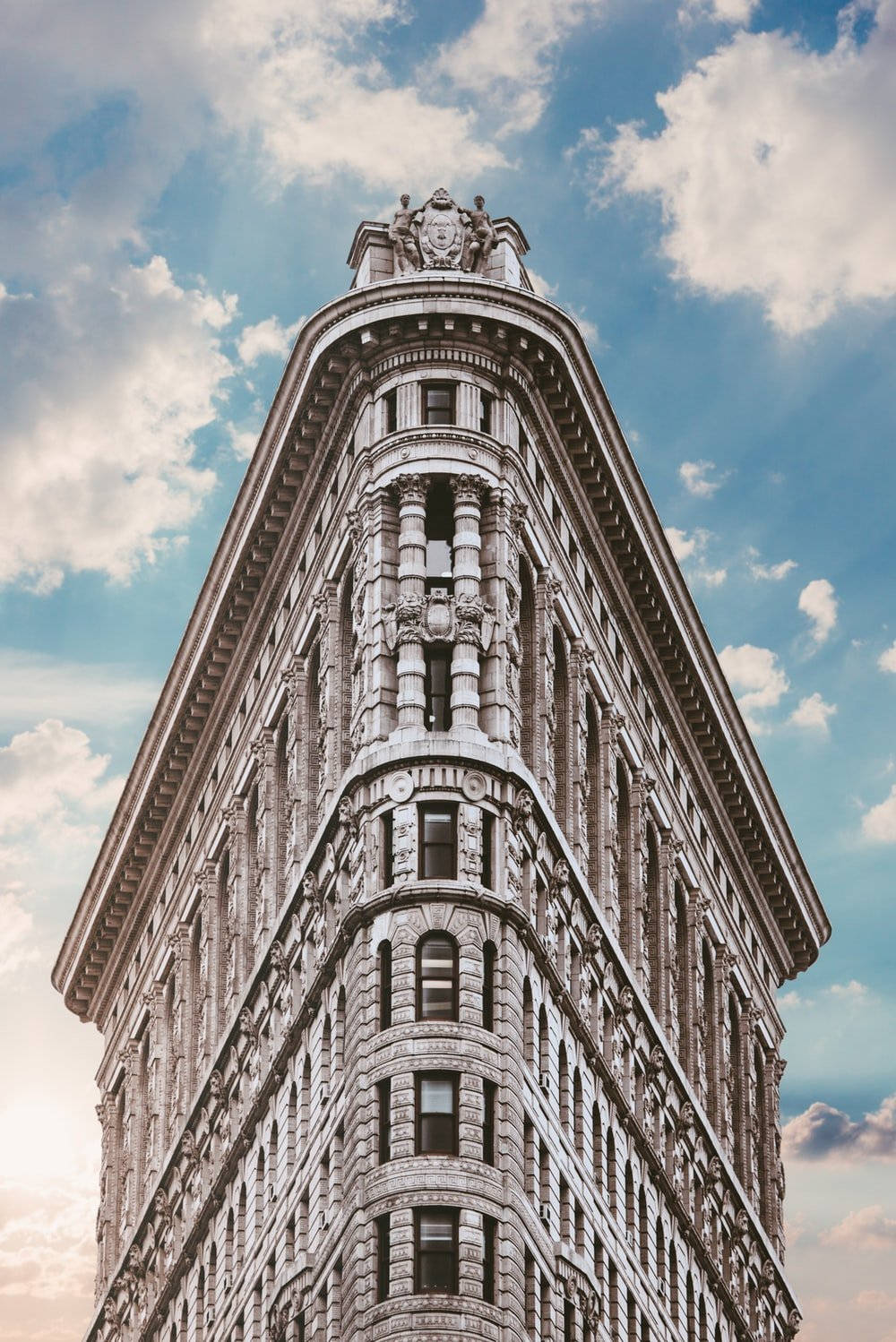 Flatiron Building 桌布 壁紙 — 從低角度觀看紐約市標誌性的熨斗大廈，背景是晴朗的藍天和蓬鬆的白雲。