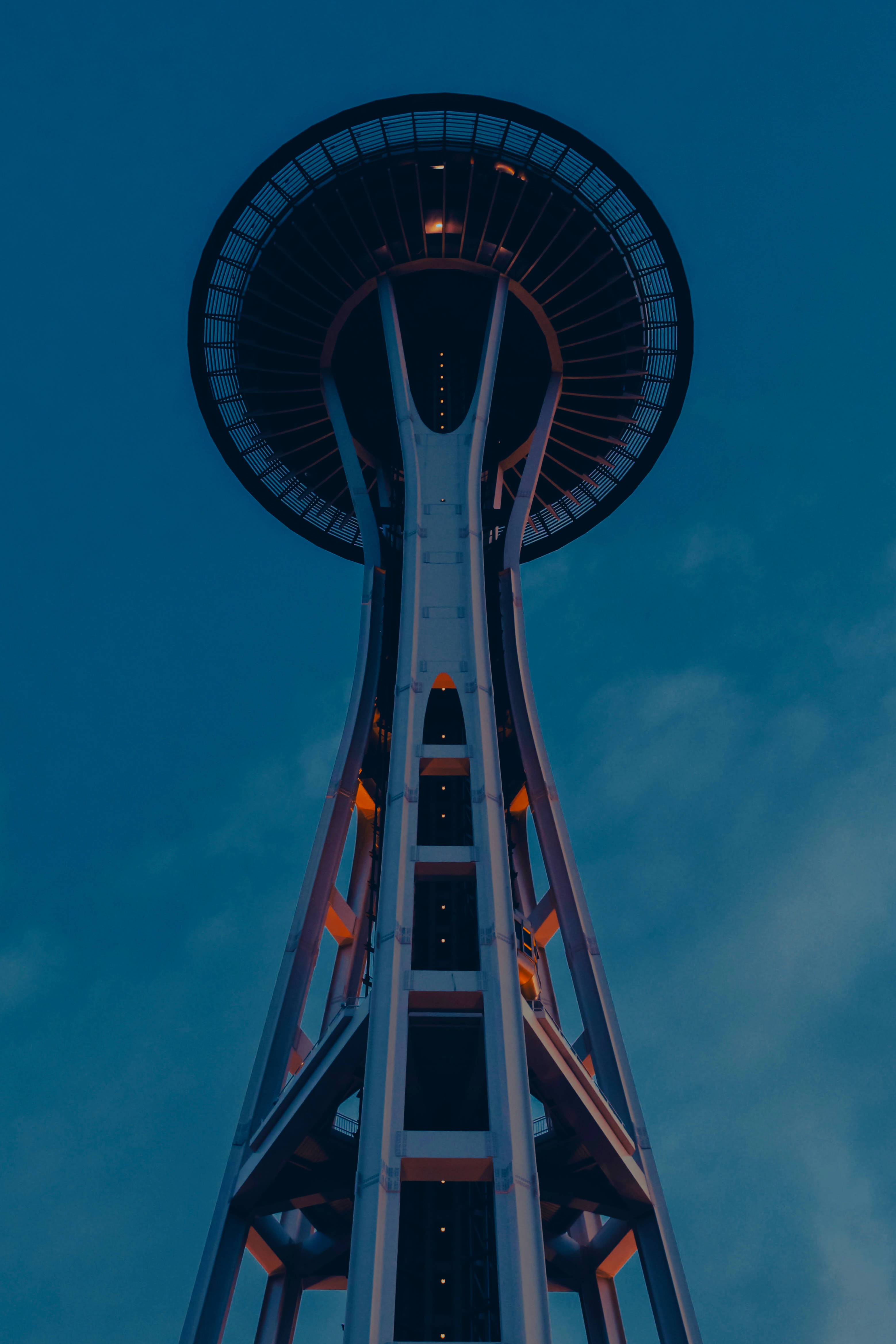 Skyscraper 桌布 壁紙 — 從低角度觀賞太空針塔在黃昏時分，溫暖的燈光在深藍色天空下閃耀。