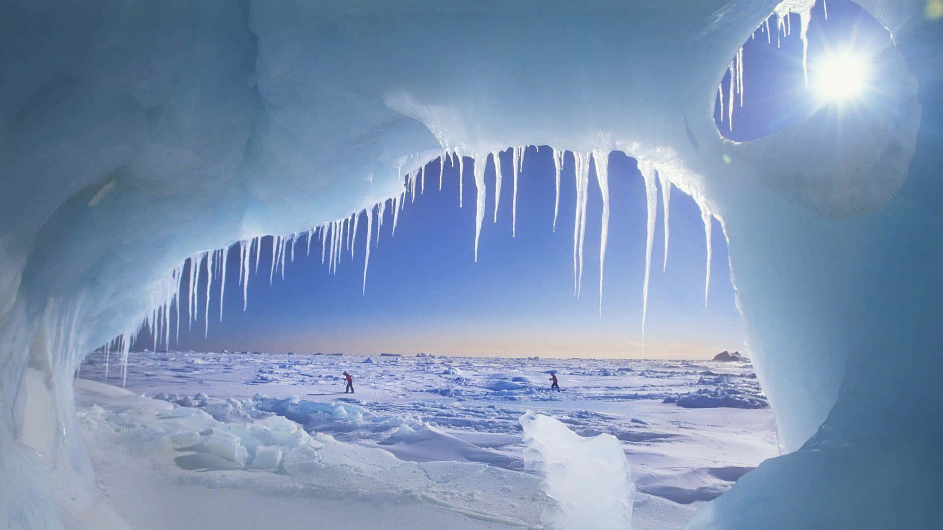 North Pole 桌布 壁紙 — 從冰洞內部欣賞的壯麗景色，冰柱懸掛在冰凍的廣闊區域上，陽光燦爛。