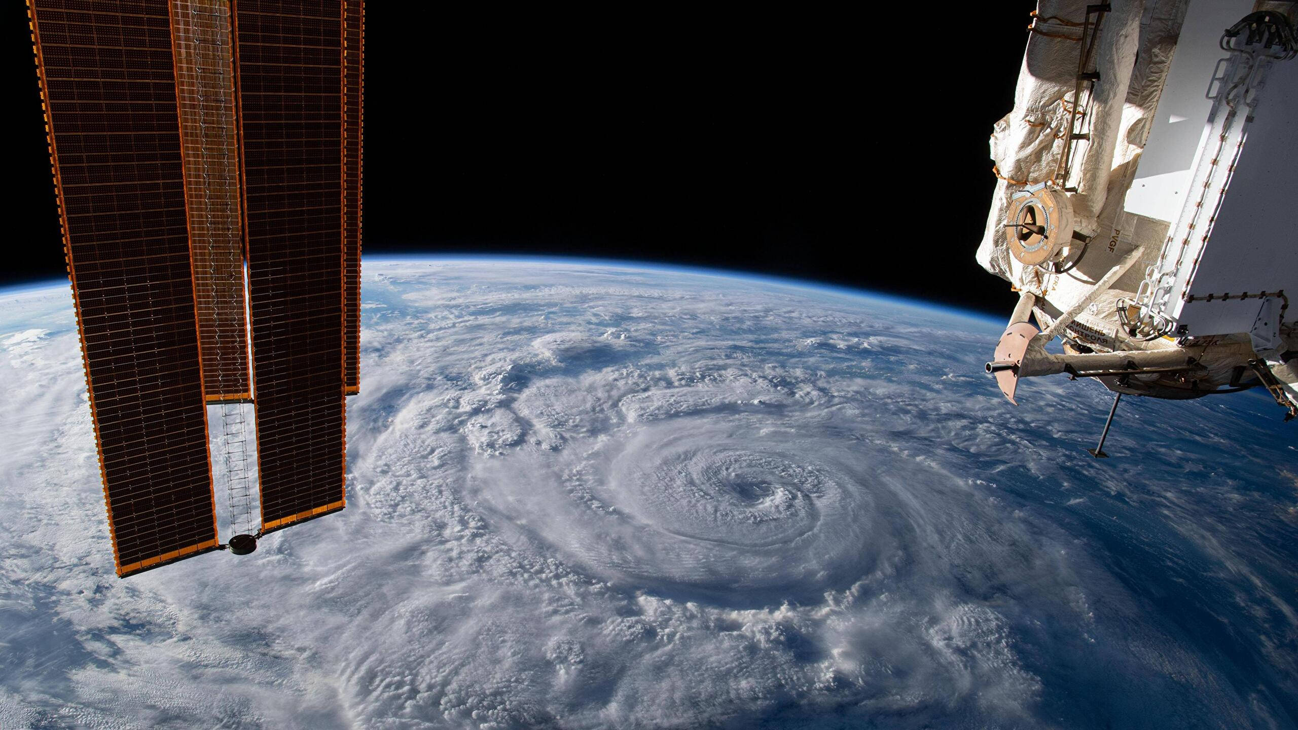 Hurricane 桌布 壁紙 — 從國際太空站看到下方一個巨大颶風旋轉，前景有太陽能板和機械臂。