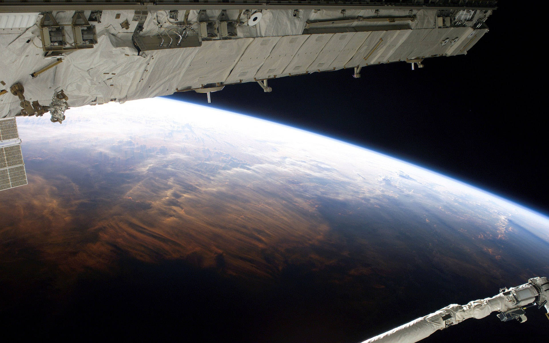 nasa 美學 桌布 壁紙 — 從國際太空站看到的壯麗景色，顯示了地球彎曲的地平線，有旋轉的雲層和棕色陸地，背景是漆黑的太空。
