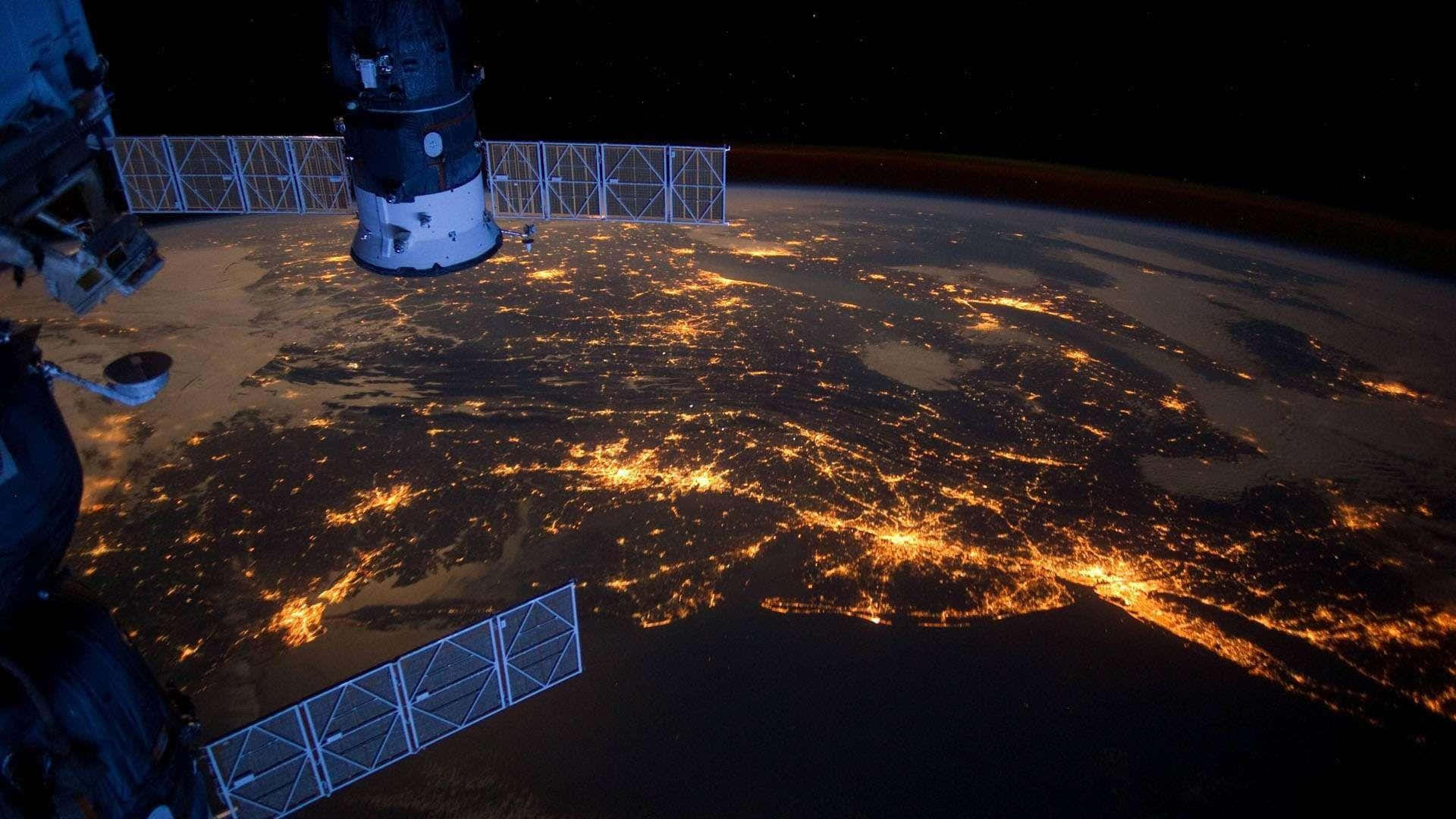 Satellite 桌布 壁紙 — 從國際太空站看到的景色顯示了地球在夜晚中，城市燈光在黑暗的海洋和陸地上閃爍。