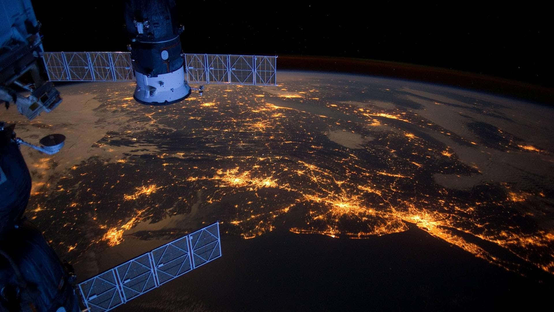 Satellite 桌布 壁紙 — 從國際太空站看到的景色顯示地球在夜間發光的城市燈光，映襯著黑暗的海洋和陸地。