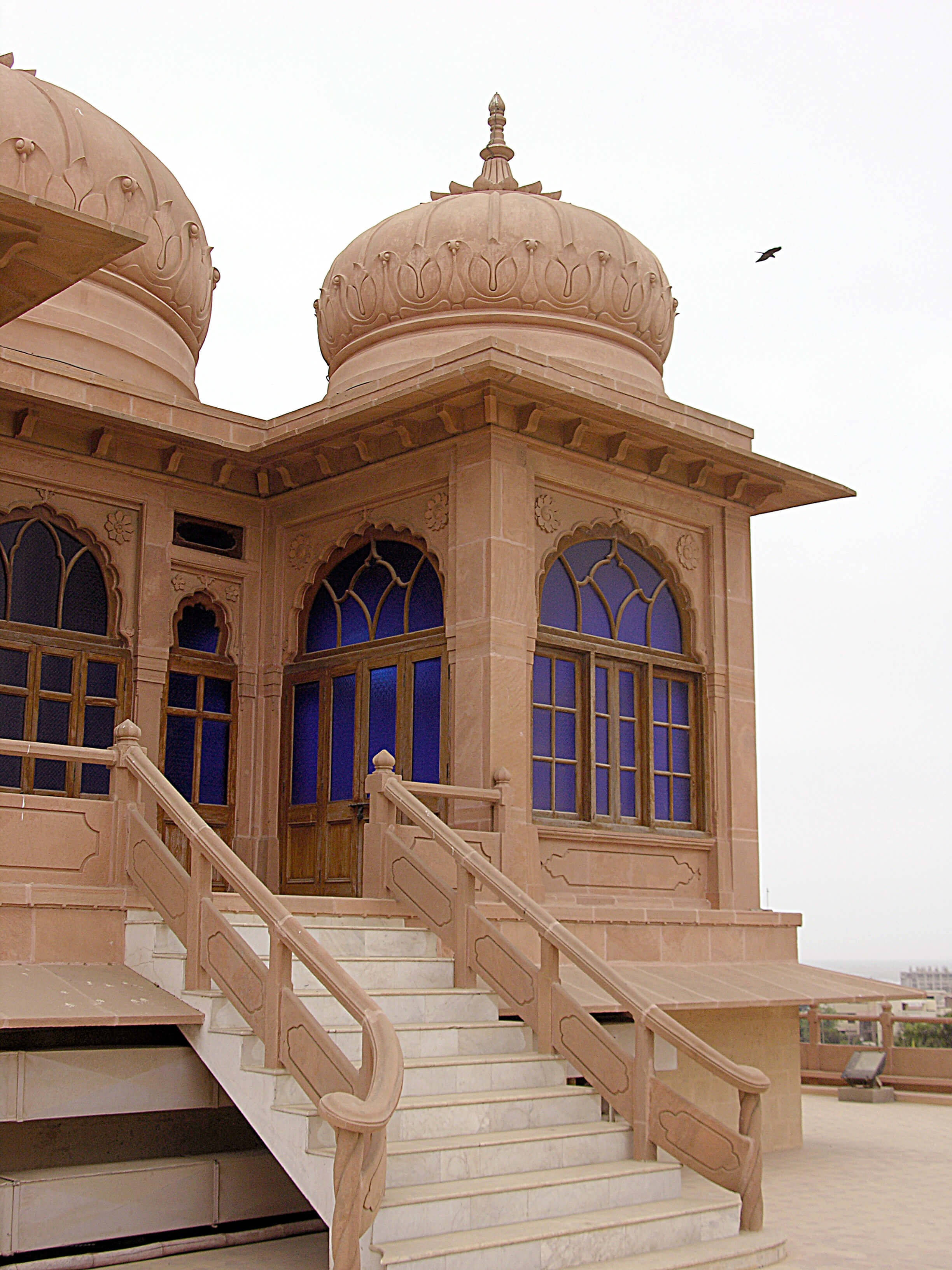 Karachi 桌布 壁紙 — 從大理石樓梯上觀看，一座宏偉的米色石建築，帶有圓頂和藍色彩繪玻璃窗，天空多雲。