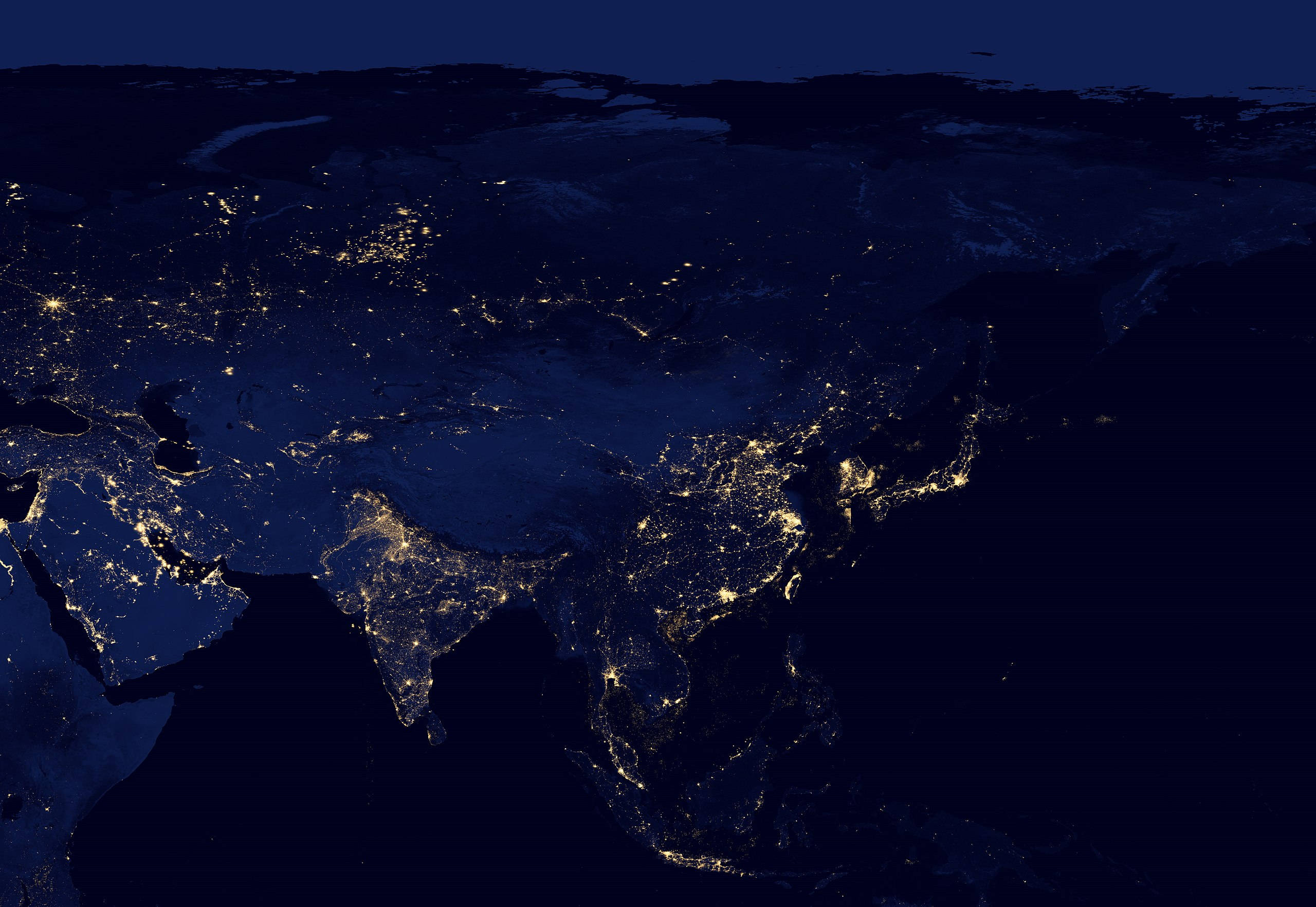 Asia 桌布 壁紙 — 從太空俯瞰地球的壯麗夜景，在深藍色背景下展現亞洲和歐洲閃爍的城市燈光。