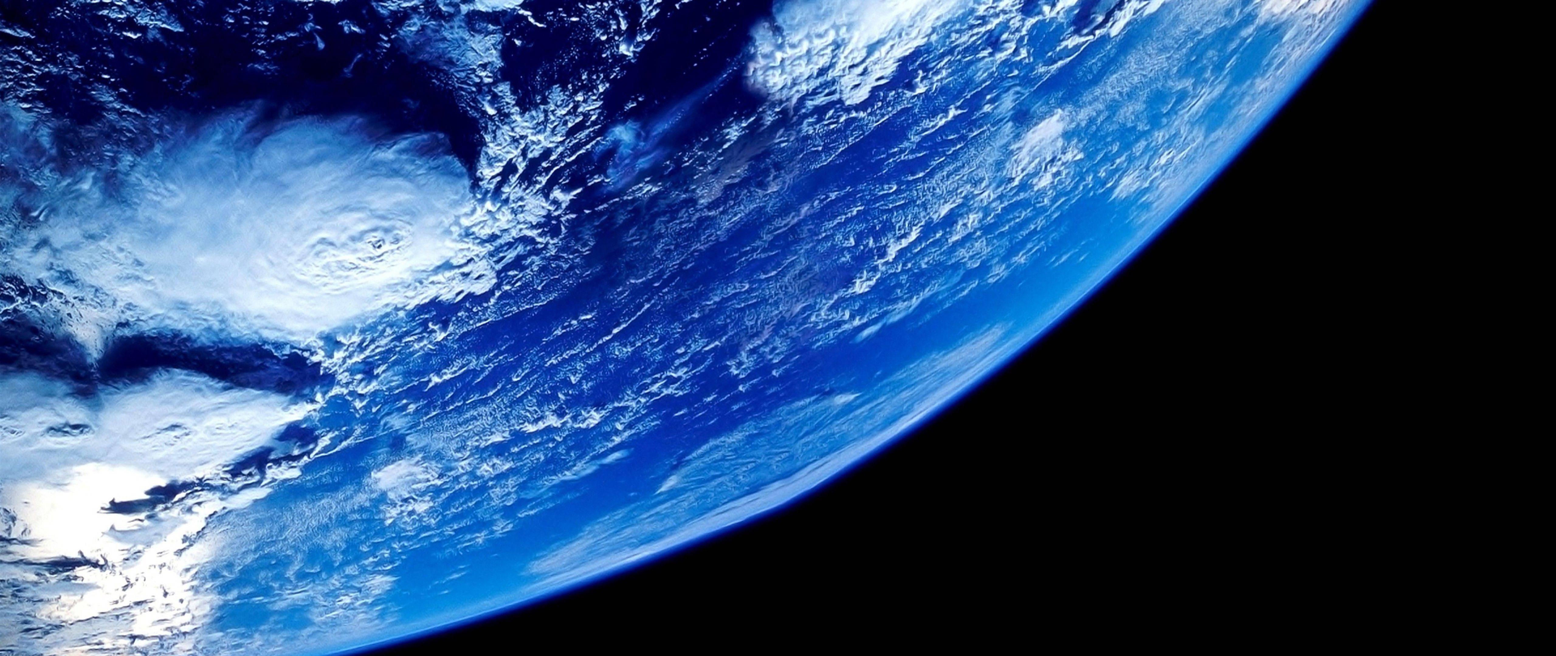 4K ultra widescreen 桌布 壁紙 — 從太空俯瞰地球的壯麗彎曲景觀，展現出鮮豔的藍色海洋和旋轉的白雲，映襯著黑色的虛空。