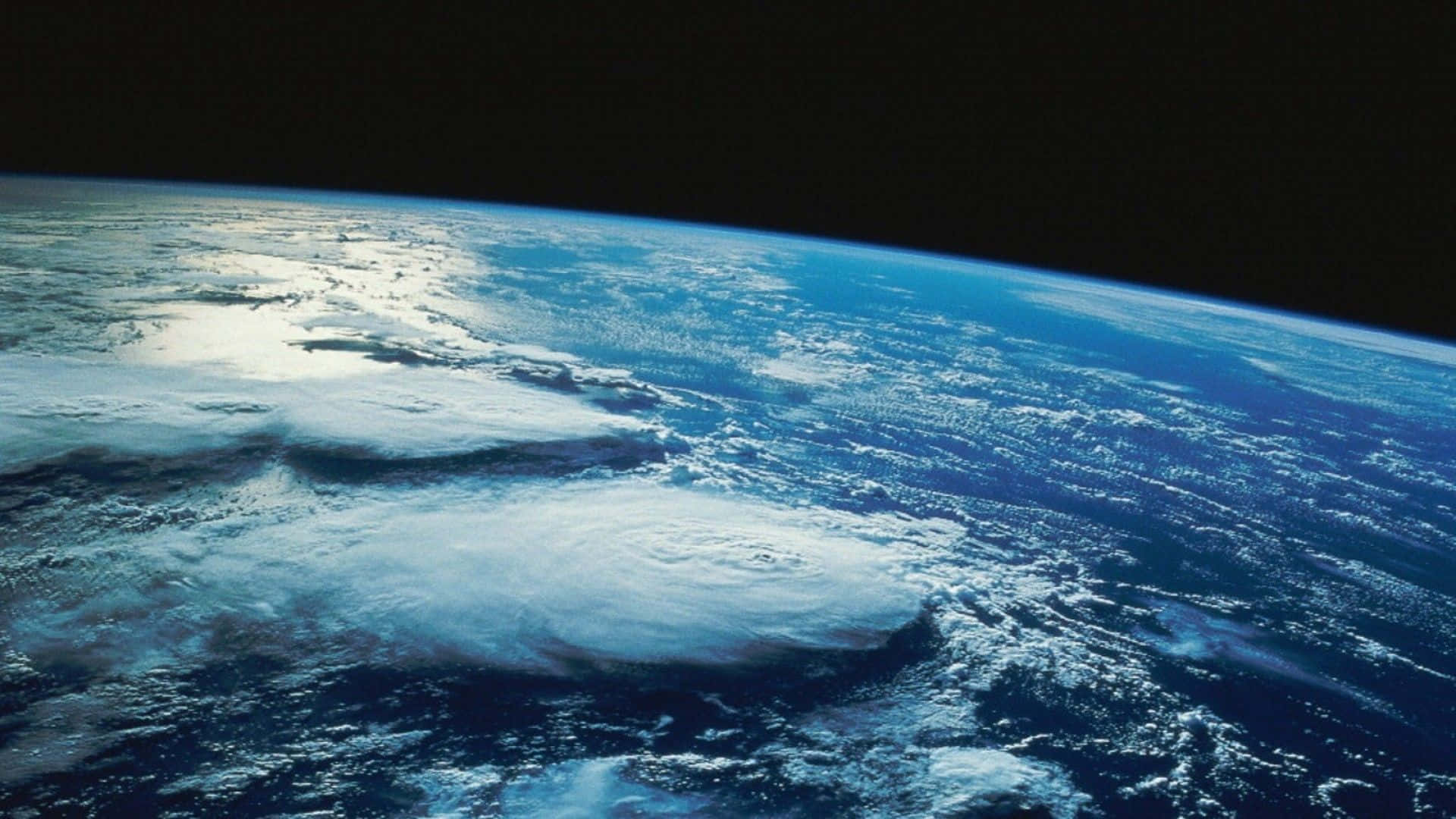 planet earth 桌布 壁紙 — 從太空俯瞰地球的壯麗景色，展現出一個巨大的颶風在深藍色海洋上空旋轉，背景是漆黑的虛空。