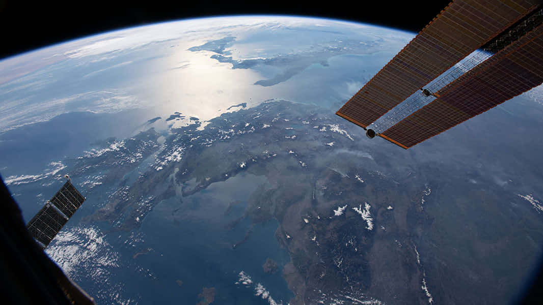 International Space Station 桌布 壁紙 — 從太空俯瞰地球的壯麗景色，顯示大陸、海洋和雲層，前景有太空船的太陽能板。