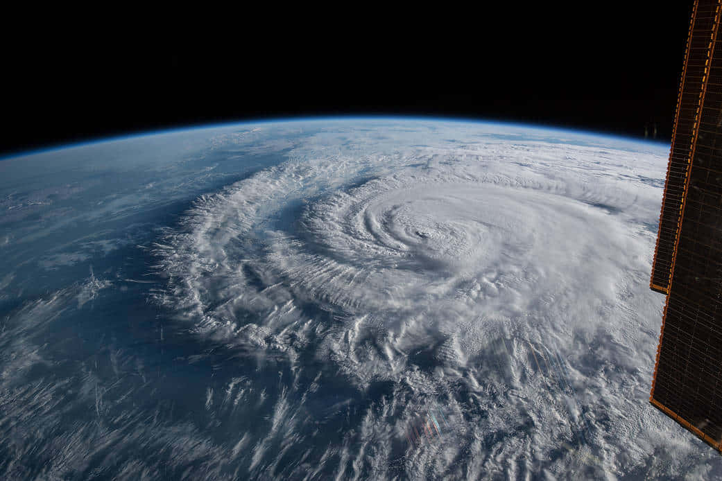 Hurricane 桌布 壁紙 — 從太空看到一個巨大颶風在地球藍色海洋上空旋轉，畫面中可見太空船的太陽能板。