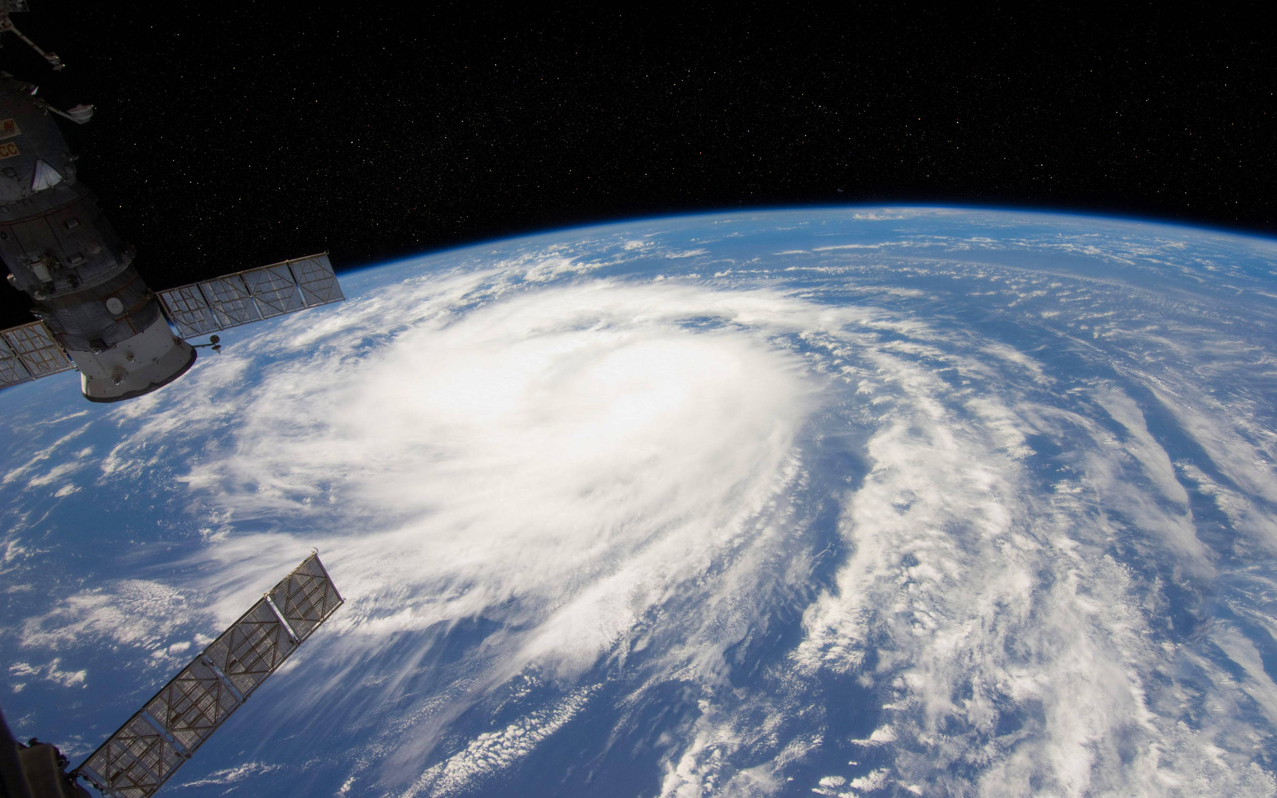 nasa 美學 桌布 壁紙 — 從太空站的角度看，一個巨大的颶風在地球的藍色海洋上空旋轉，太陽能板延伸至星空虛空。
