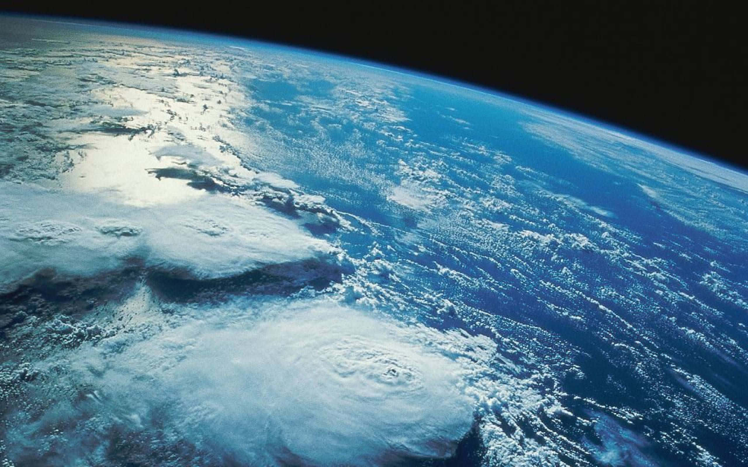 Earth Science 桌布 壁紙 — 從太空觀看，一個旋轉的颶風主宰著一個擁有白雲和深色海洋的藍色星球。