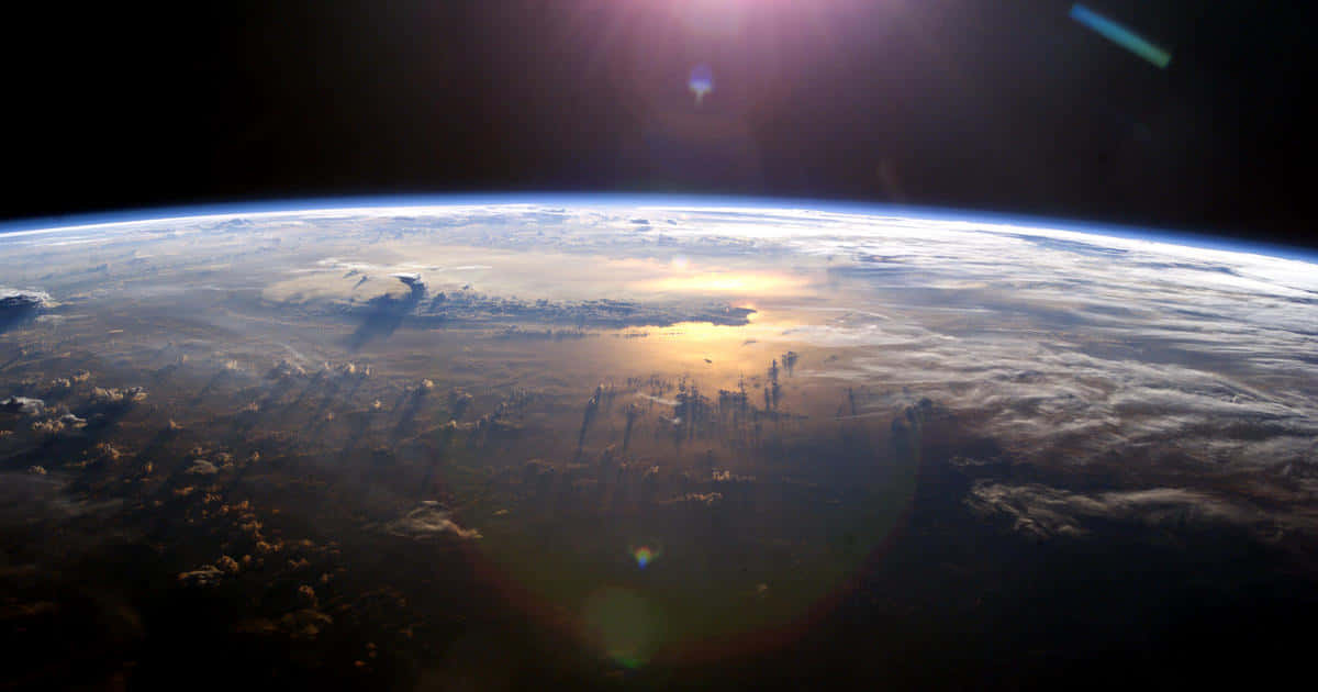 太空 桌布 壁紙 — 從太空觀看地球，太陽耀斑將金色光芒投射在旋轉的雲層和藍色大氣層上。