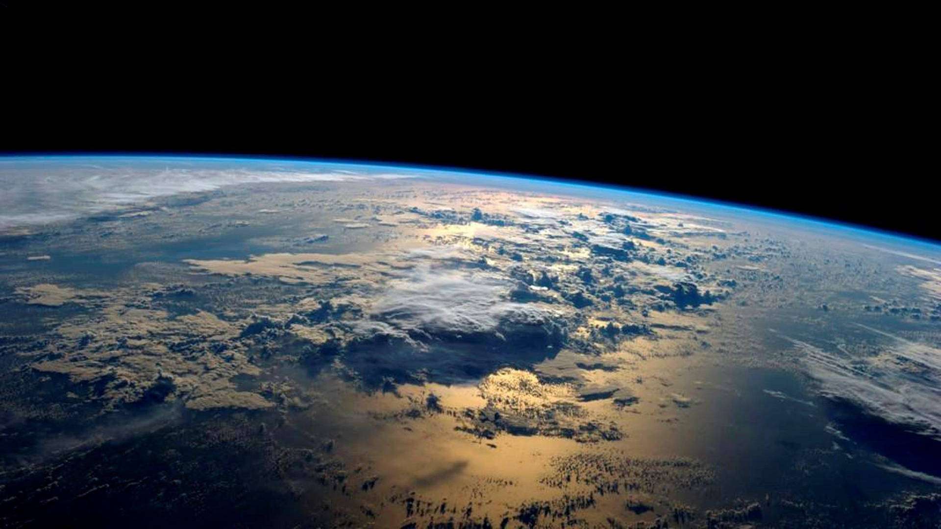 地球 桌布 壁紙 — 從太空觀看地球，金色陽光照射著旋轉的雲層，映襯著深藍色曲線和黑色虛空。