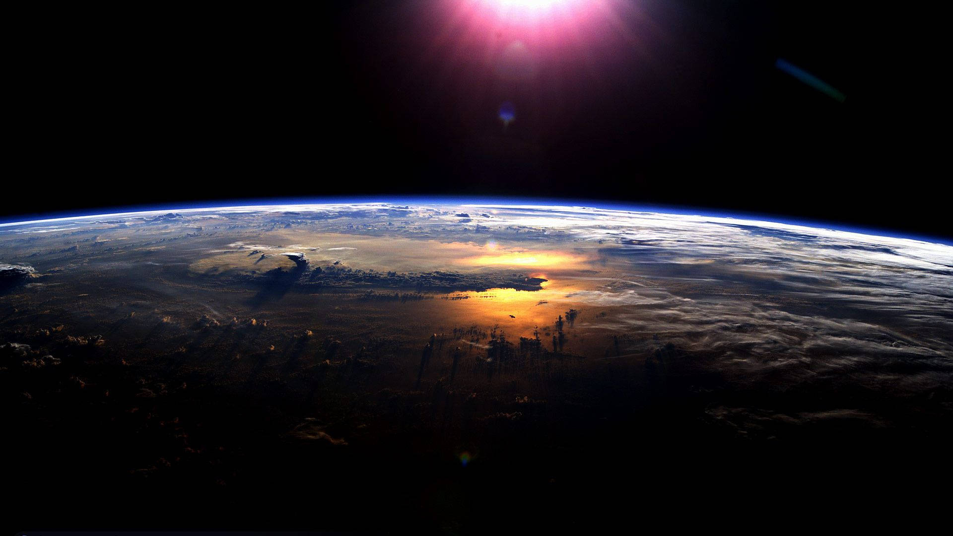 地球 桌布 壁紙 — 從太空觀看地球日出，雲層上呈現鮮豔橙色光芒和藍色大氣曲線。