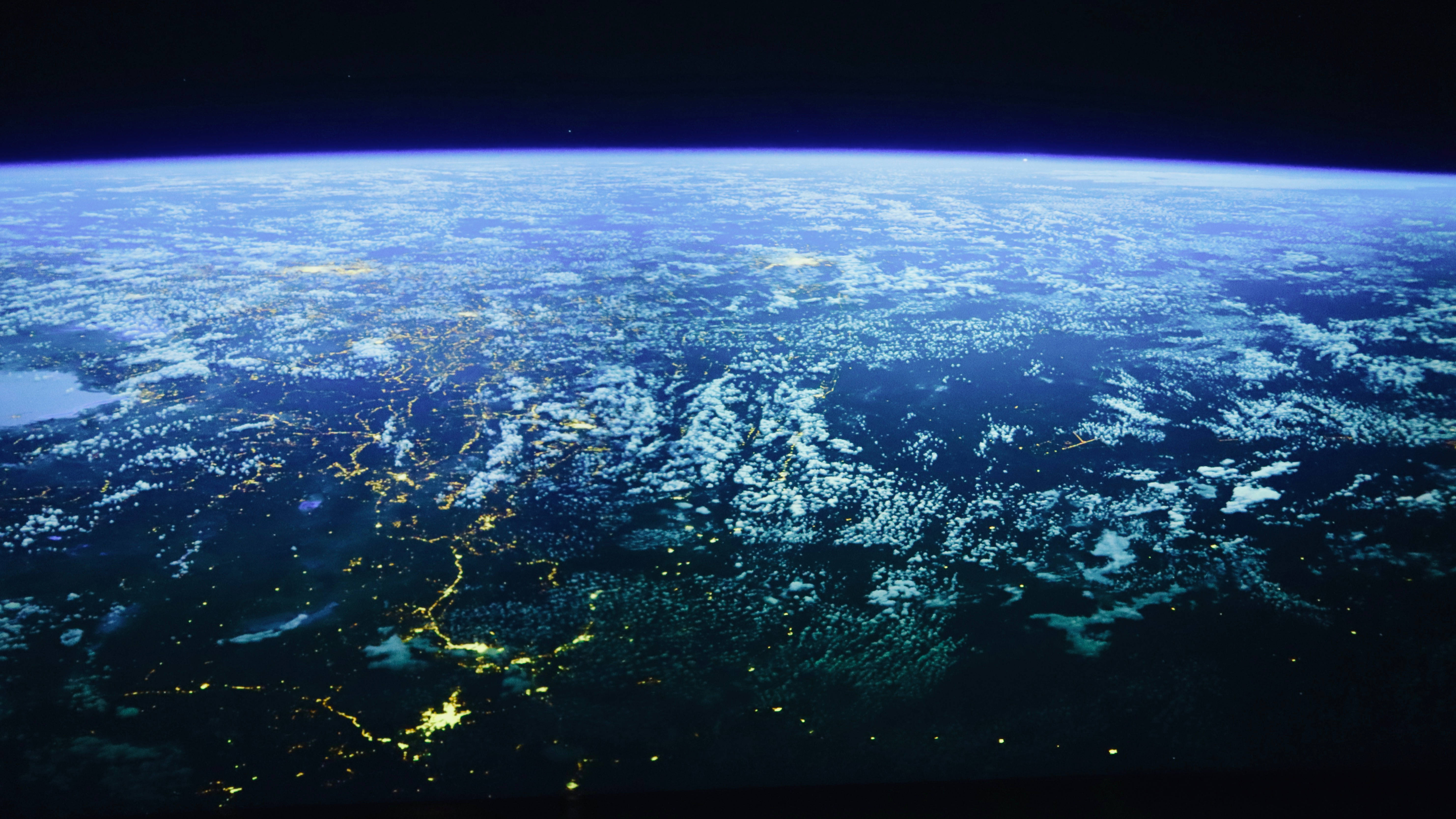 Civilization Beyond Earth 桌布 壁紙 — 從太空觀看夜晚的地球，城市燈光閃爍，雲層旋轉，背景是黑暗的宇宙。