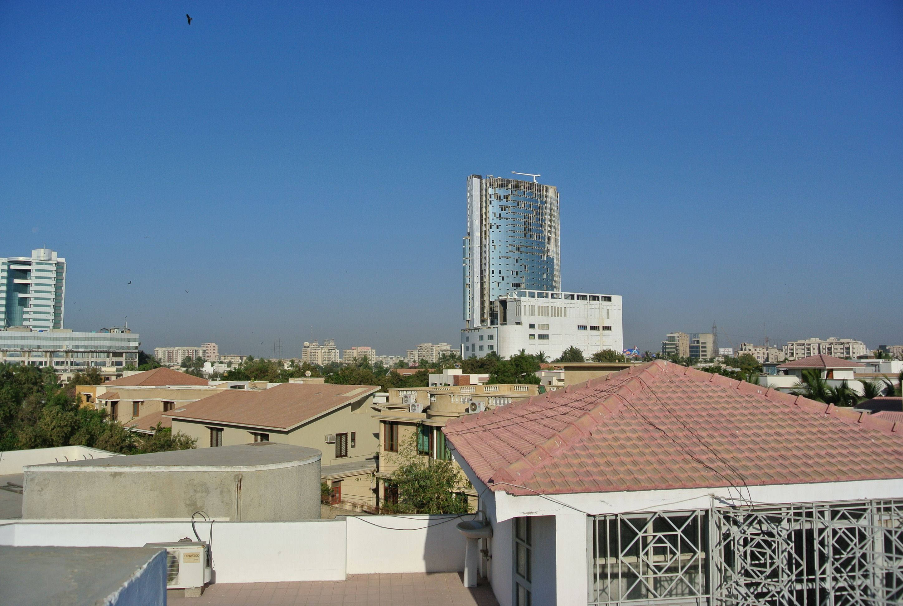 Karachi 桌布 壁紙 — 從屋頂俯瞰城市景觀，紅瓦屋頂和高聳的玻璃摩天大樓在清澈的藍天下。