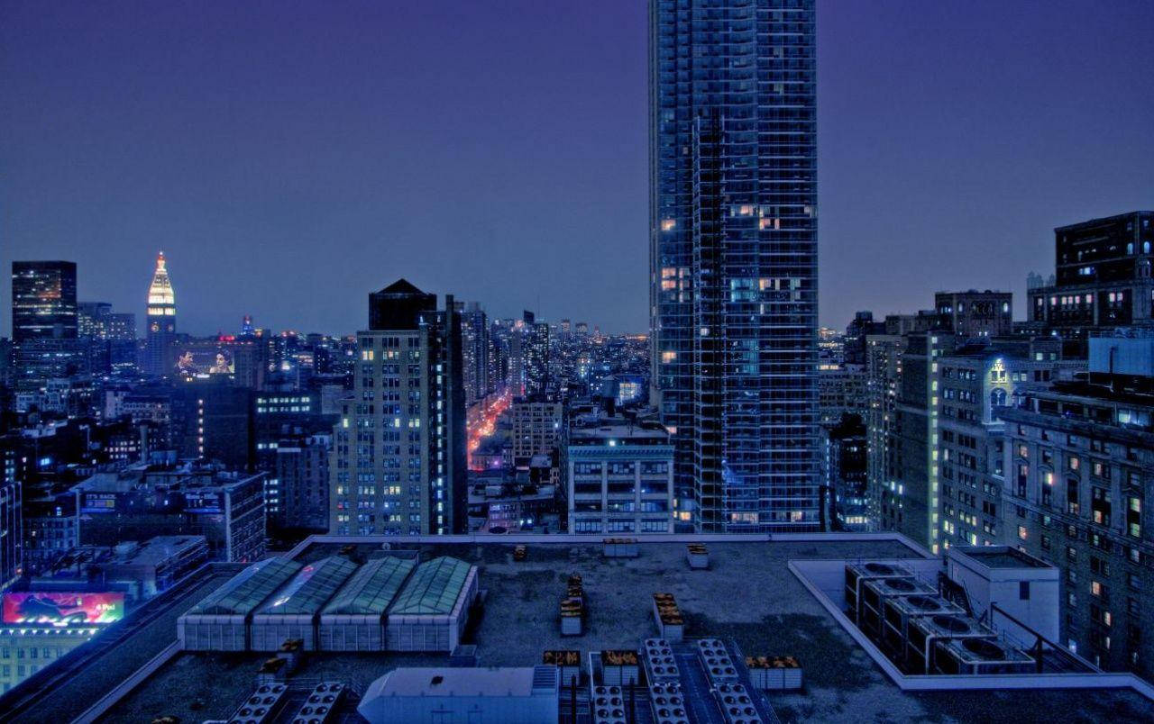Rooftop 桌布 壁紙 — 從屋頂俯瞰夜晚的廣闊城市，高聳的摩天大樓和發光的窗戶映襯著深藍色的天空。